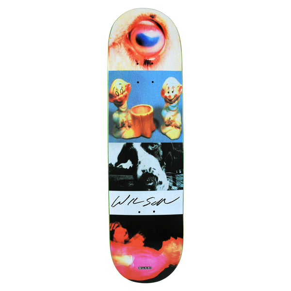 Quasi Wilson Smear skateboard deck: A collage of stacked photo strips: a close-up eye, two ceramic dwarf figurines either side of a tree stump, a black-and-white dog's face, and a blurred red-pink figure. A white band across the middle carries a handwritten signature.