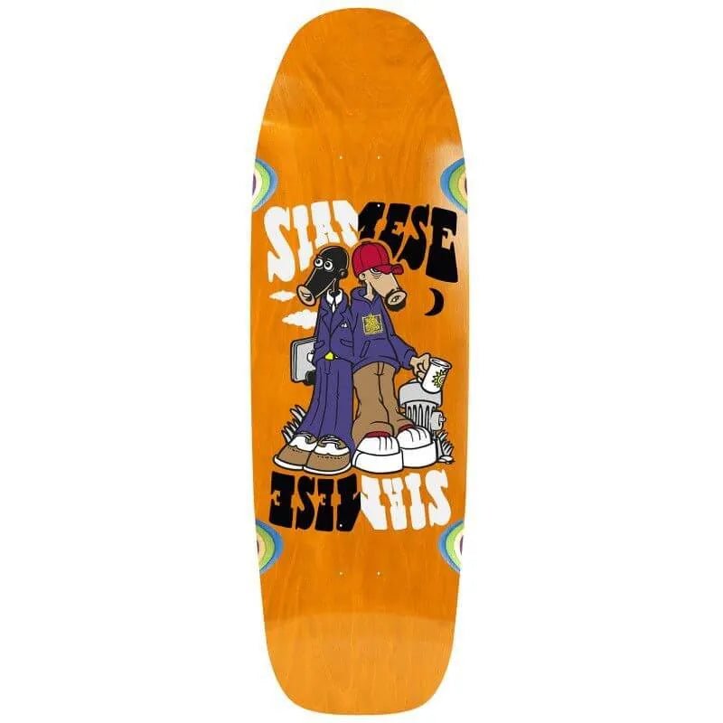 New Deal Siamese skateboard deck: Two cartoon figures standing back to back, one with a black animal head in a purple suit holding a briefcase, the other in a red cap and hoodie holding a cup, under mirrored 'Siamese' lettering. Orange old-school deck with eye shapes at the edges.