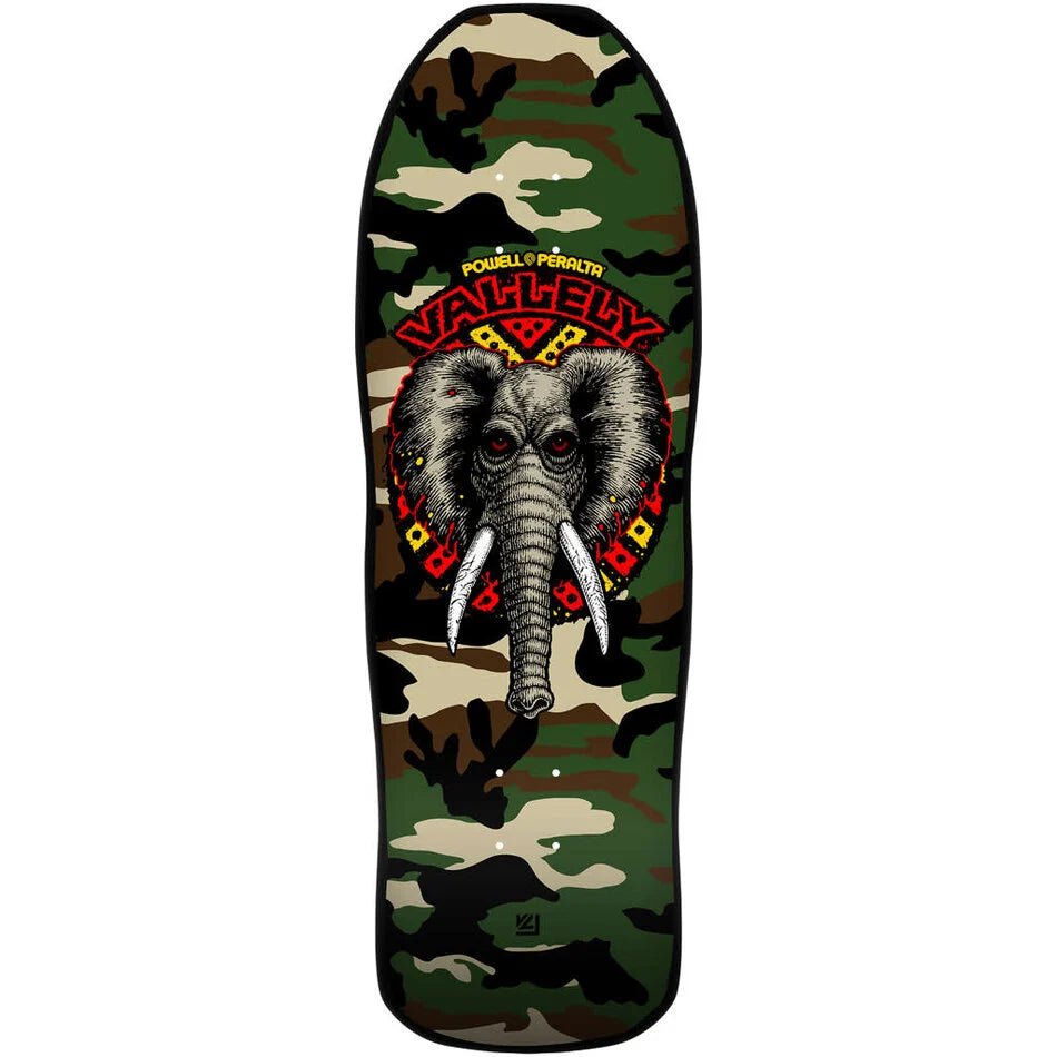 Powell Peralta Mike Vallely Elephant Camo skateboard deck: A grey elephant head with white tusks and red eyes sits within a red and yellow tribal burst, with the rider's name arched above. The deck has a green and brown woodland camouflage pattern.