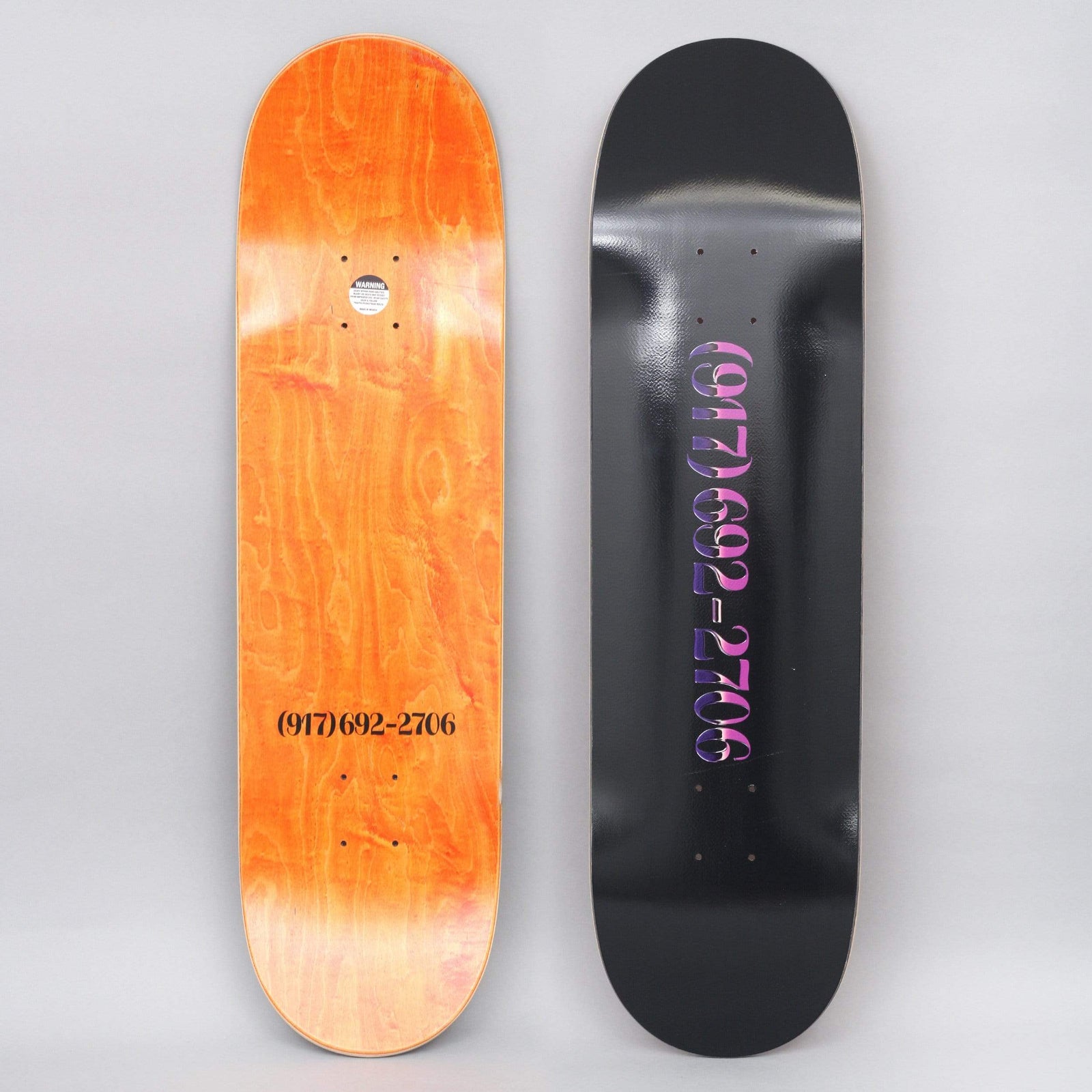 917 17 8.5 Chrome Dialtone Slick Black skateboard deck: Black slick deck with a telephone number in a purple-to-pink chrome gradient serif type. The other deck shows the same number in black on an orange stained underside.