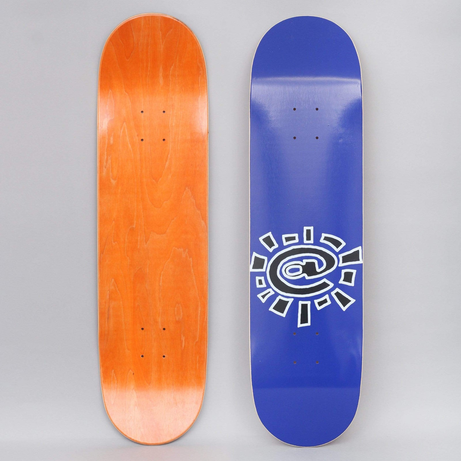 Always @Sun Navy skateboard deck: Navy blue deck with a large black and white outlined @ symbol drawn as a sun, with rays around it, placed low on the board. The underside shows orange-stained wood.