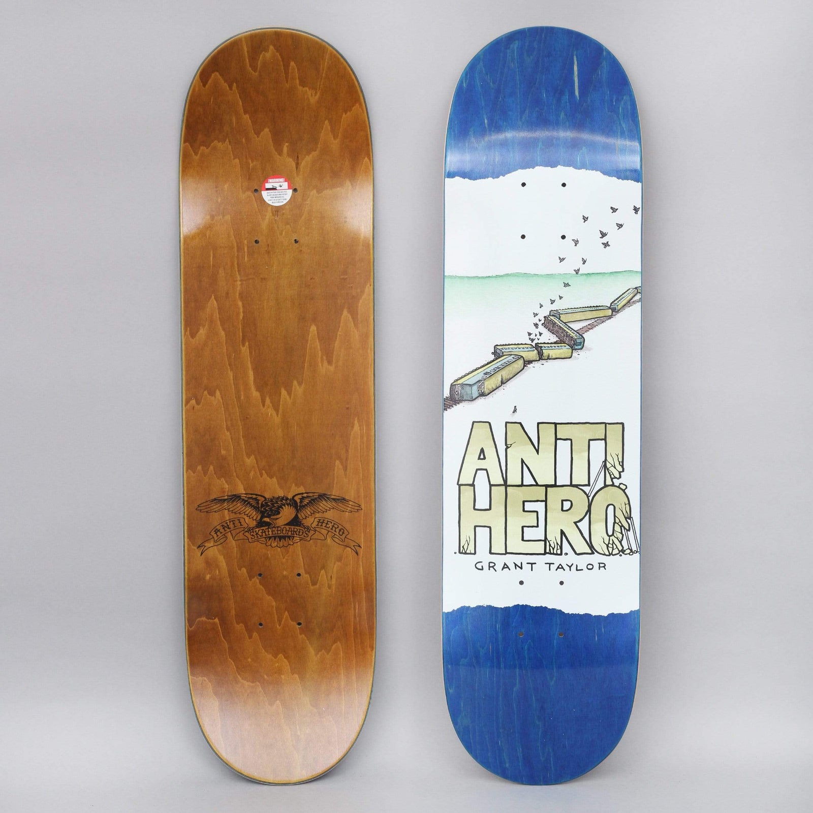 Anti Hero Grant Expressions skateboard deck: Watercolour-style scene of a derailed train snaking across a green landscape with a flock of birds above, over large stencil-style brand lettering and the rider's name, on a white panel with torn edges. Blue-stained deck, with the brown underside showing an eagle.