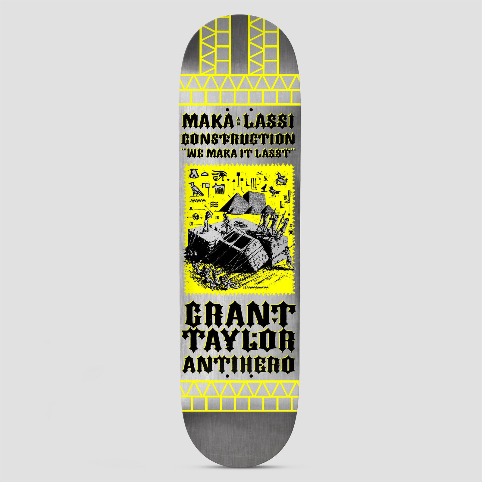 Anti Hero Grant Makalassi Construction Re-Color DBX Silver skateboard deck: Silver deck with yellow brick-pattern borders and a yellow panel showing a line drawing of workers hauling a large block near pyramids with hieroglyphs. Black blackletter text above and below.