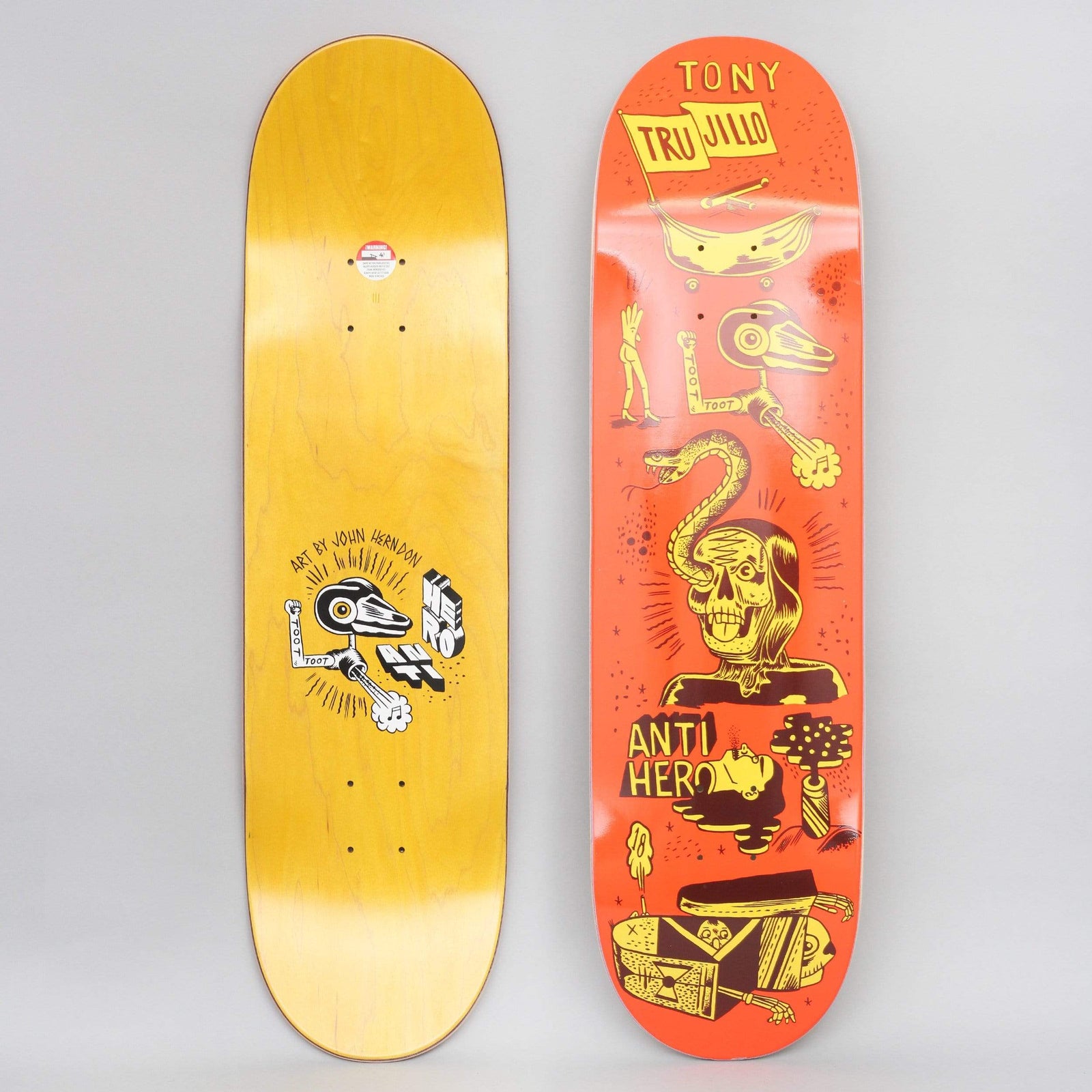 Anti Hero Trujillo Reach For The Stars Orange skateboard deck: Orange deck with yellow and maroon drawings of a skull-faced figure with a snake, a robotic arm tooting, a banana-like boat with a flag, a severed head and a coffin. Tony Trujillo in the flag, Anti Hero lettered. Underside shows Art by John Herndon.