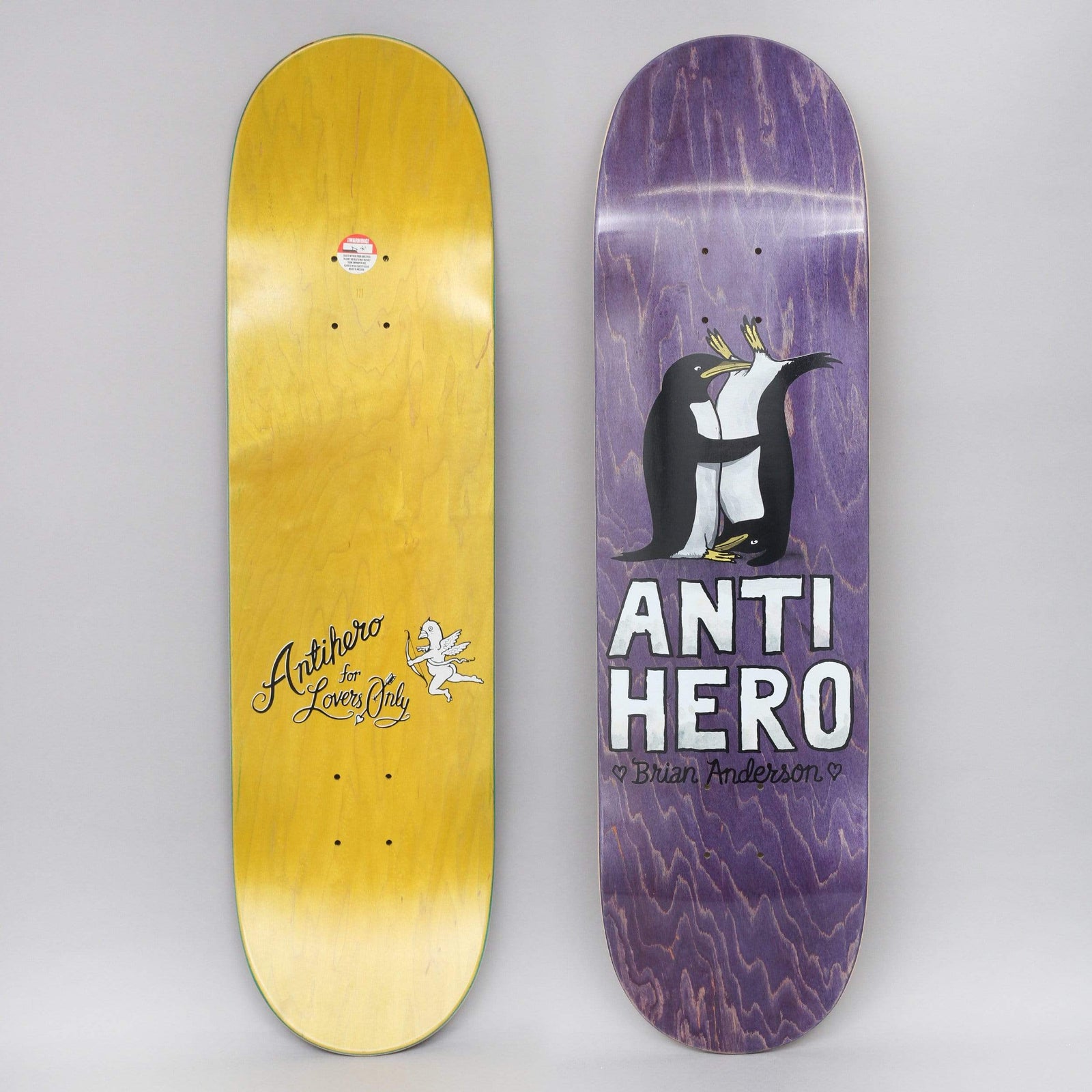 Anti Hero B.A. Lovers II skateboard deck: Two penguins embracing with a small one at their feet, above big white Anti Hero lettering and the name Brian Anderson, on purple stain. The yellow underside shows a cupid and For Lovers Only script.