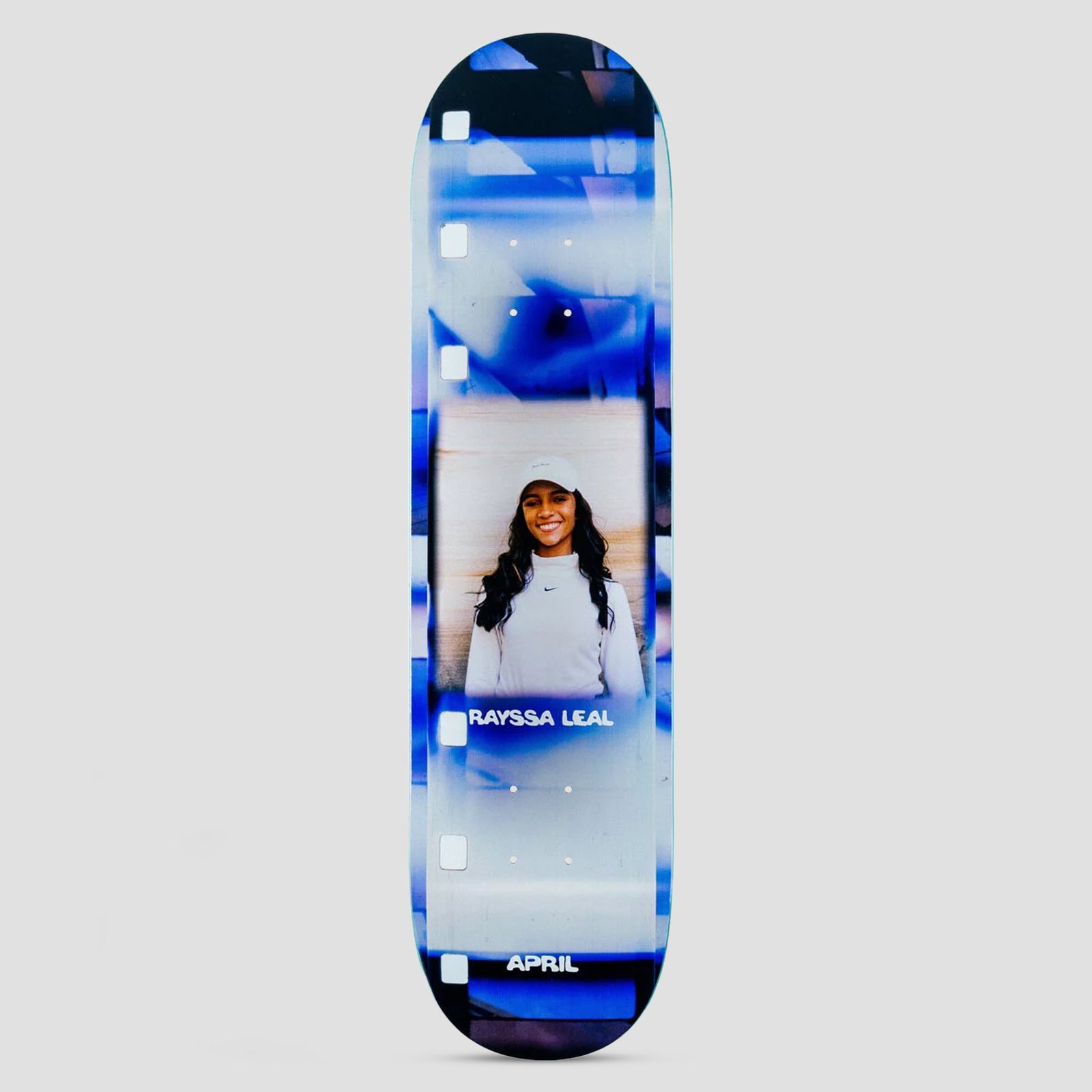 April Rayssa Leal 2023 skateboard deck: Photo of a smiling woman with long dark hair in a white cap and top, framed by a blurred blue and white film-strip border with sprocket holes. Rider name and APRIL appear on the deck.