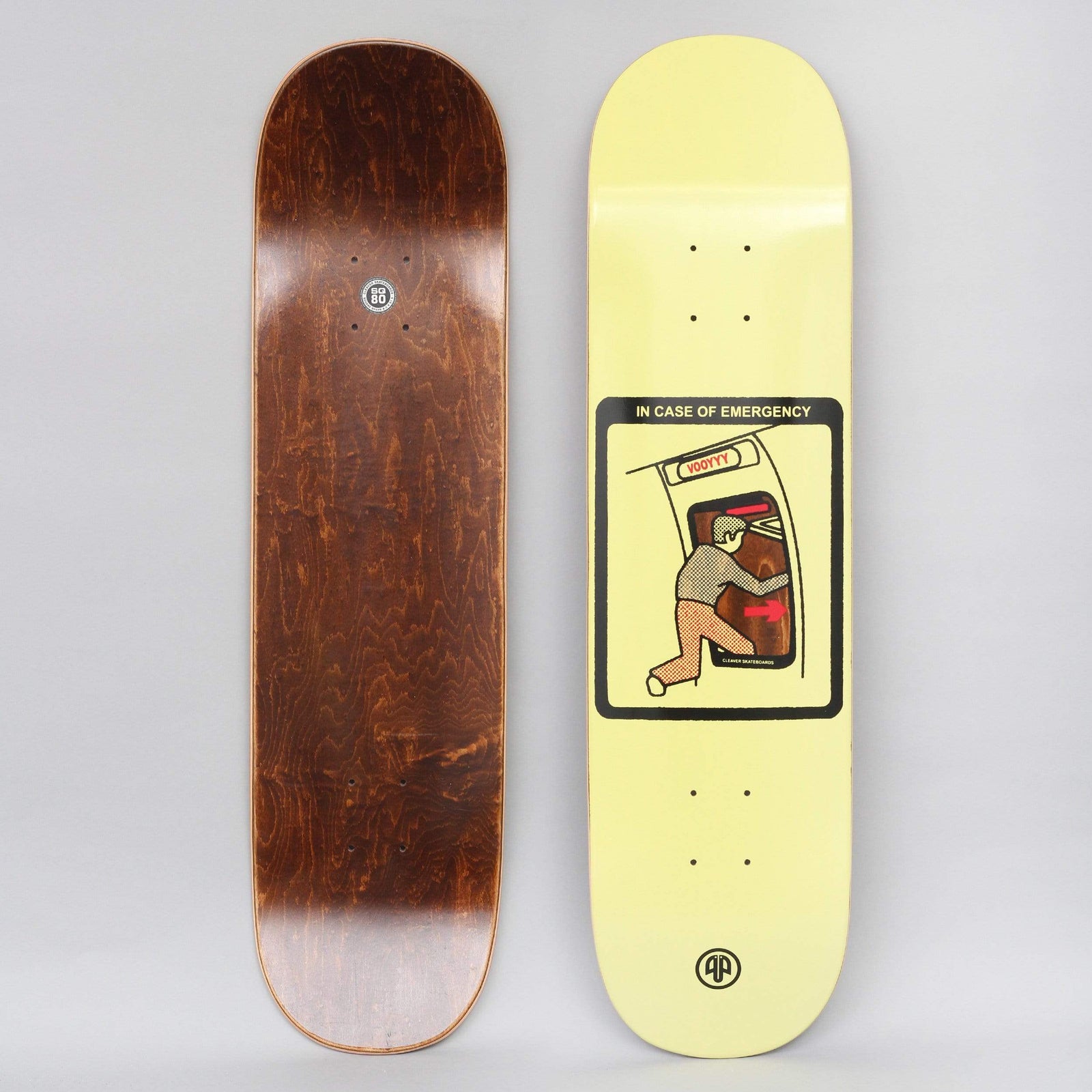 Cleaver Emergency Yellow skateboard deck: A safety-card style illustration of a man pushing open a plane's emergency exit door, with a red arrow and a labelled hatch, in a rounded black frame on a pale yellow deck. A small logo sits at the tail; the brown-stained underside is shown.