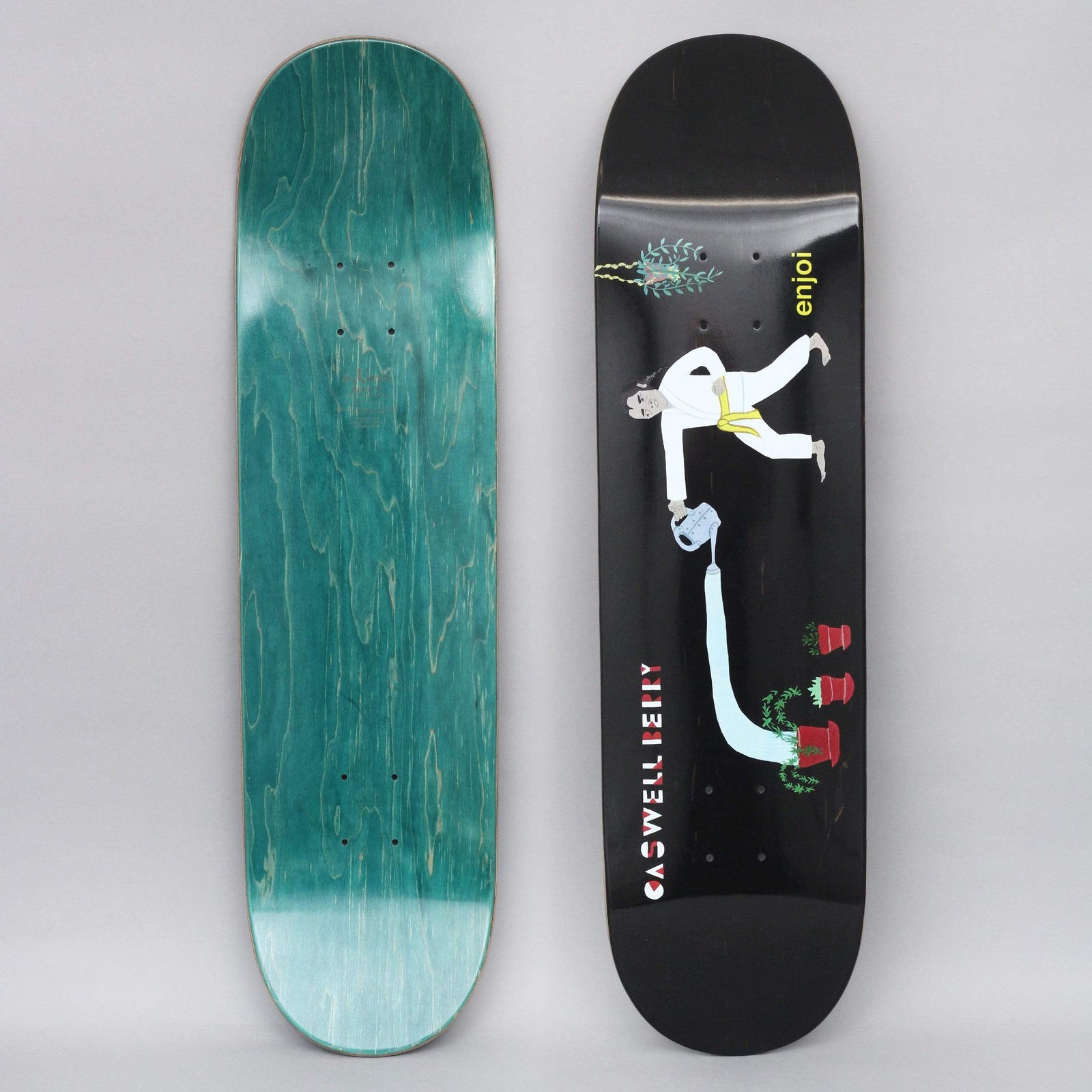 Enjoi Caswell Over Board R7 Black skateboard deck: Illustration of a man in a white karate suit with a yellow belt, leaning over to pour water from a can in a long stream into red plant pots. A hanging plant sits at the top, on a plain black ground.