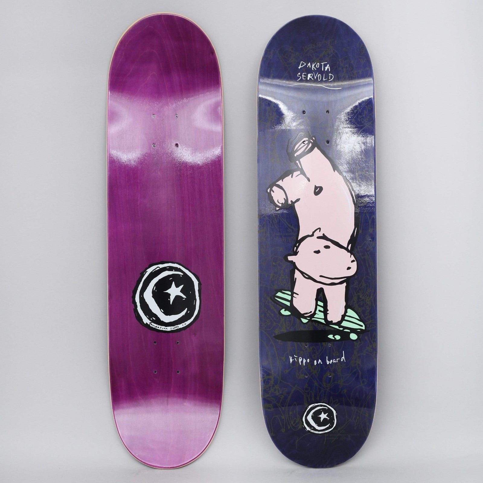 Foundation Servold Hippo skateboard deck: Naive drawing of a pink hippo balancing upside down on a green skateboard on a navy deck with faint scribbles. Dakota Servold name written at the top and hippo on board caption beside; Foundation star and moon logo at the tail. Bottom view shows purple stain with large logo.