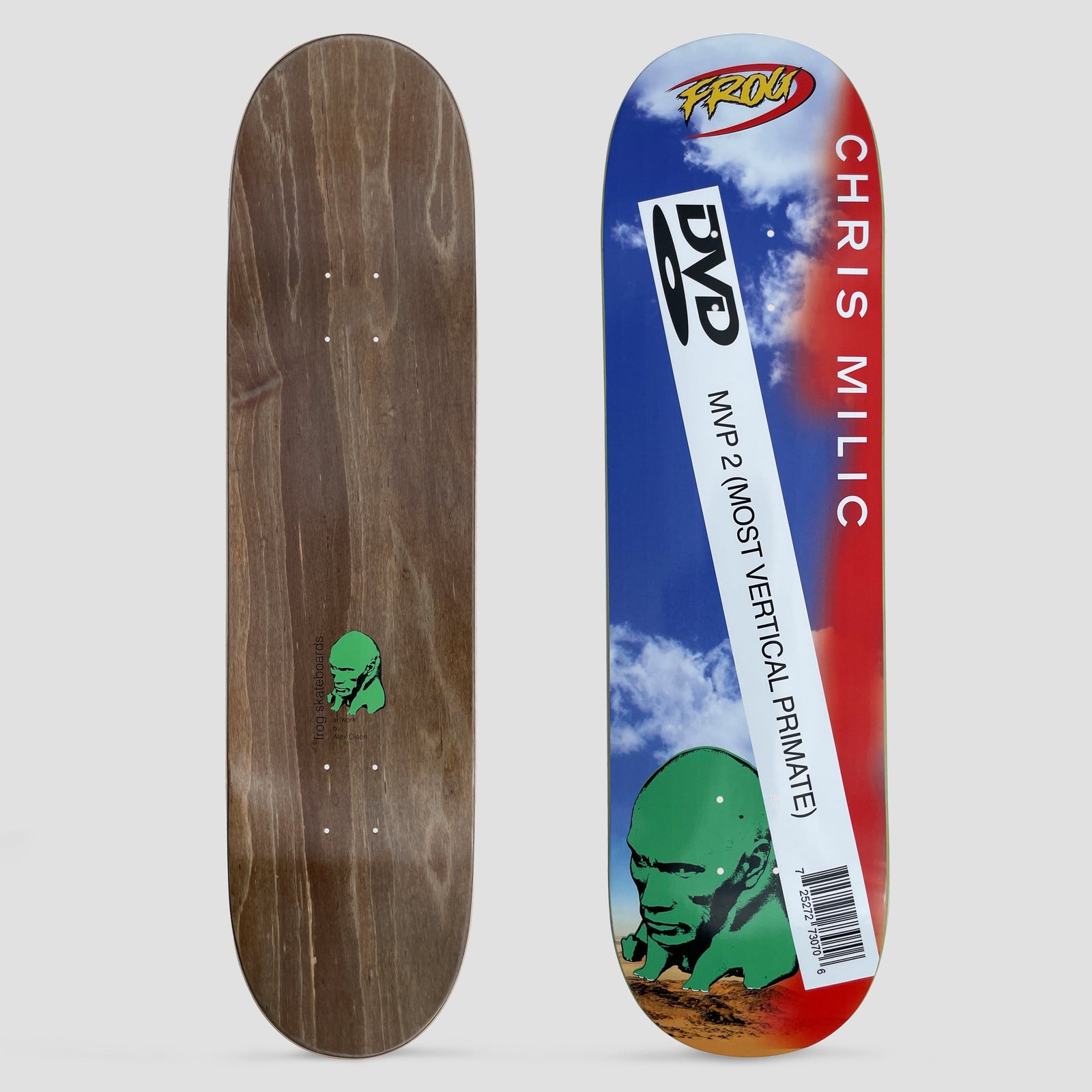 Frog Chris Milic Dwayne skateboard deck: A green stone-like head sunk in desert sand below a blue sky with clouds, with a white DVD-case style label reading MVP 2 (MOST VERTICAL PRIMATE) and a barcode across it. CHRIS MILIC runs in white down a red edge, with a Frog logo at the top.