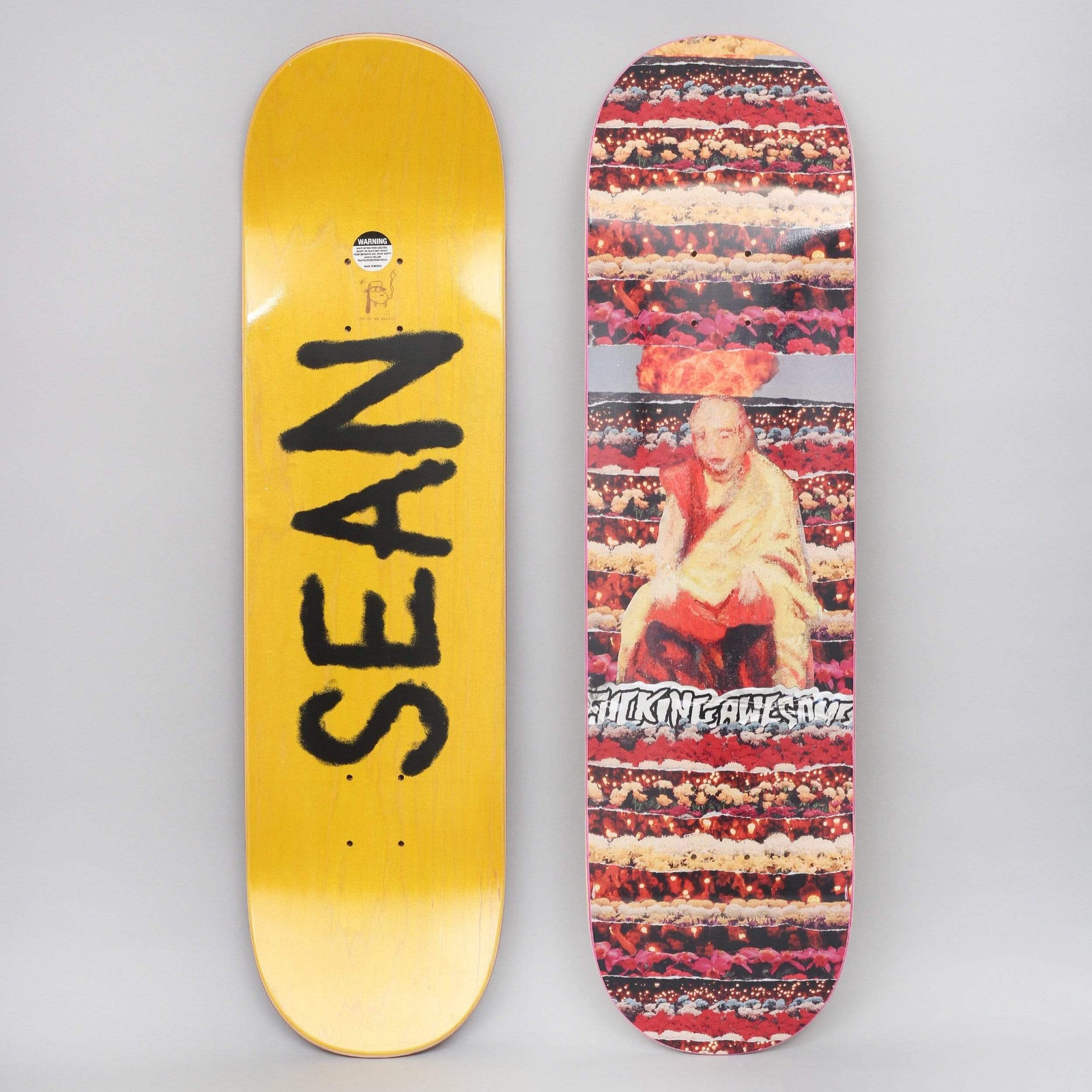 Fucking Awesome Sean Buddha skateboard deck: Painted figure of a seated robed monk with flames above his head, set over banded rows of red and pink flowers and candles, with a scratchy logo. Underside has 'SEAN' sprayed in black on yellow.