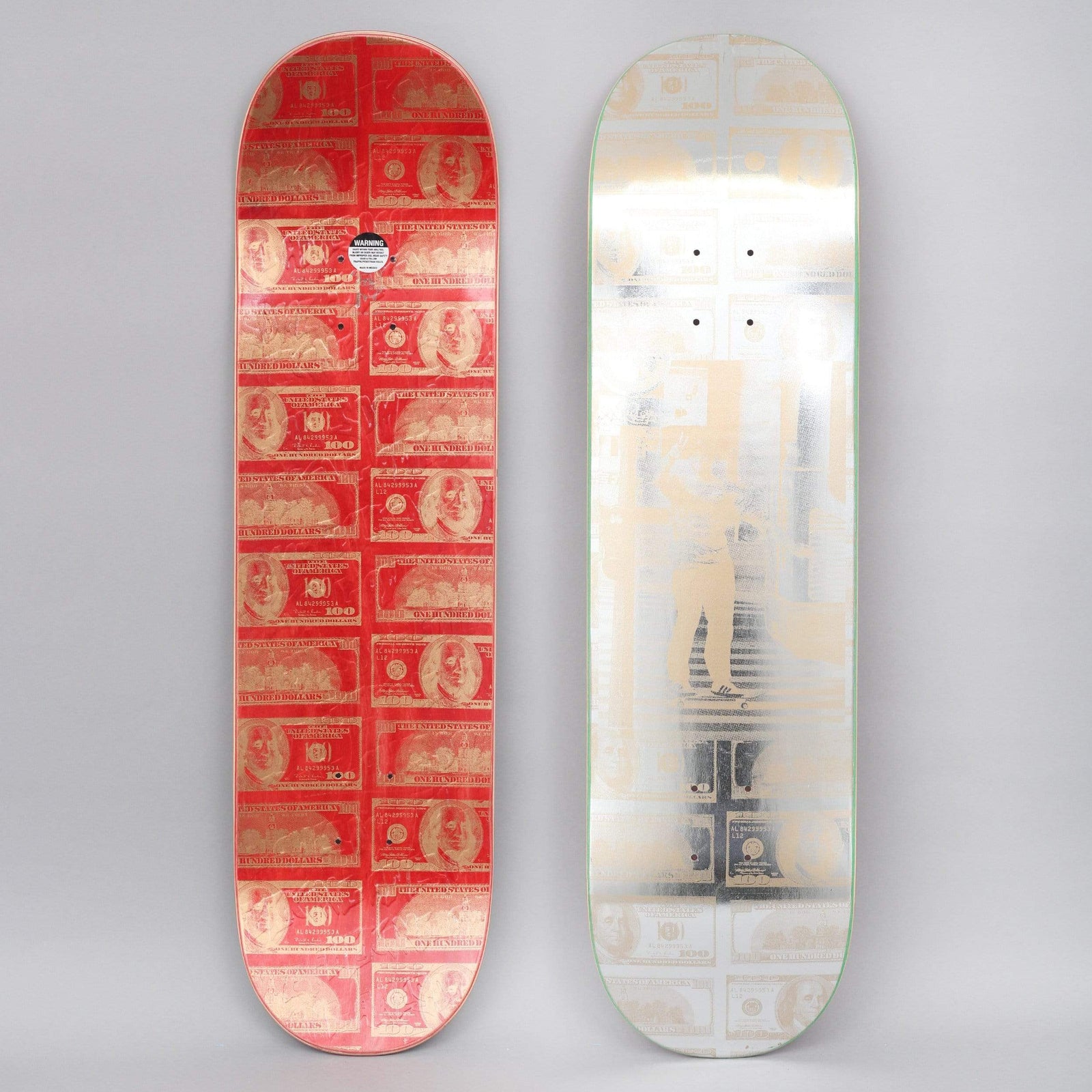 Fucking Awesome Tyshawn Peace Out Gold skateboard deck: A grid of repeated dollar bills in gold on a red deck, shown alongside a silver foil deck with a ghosted dollar pattern and a standing figure.