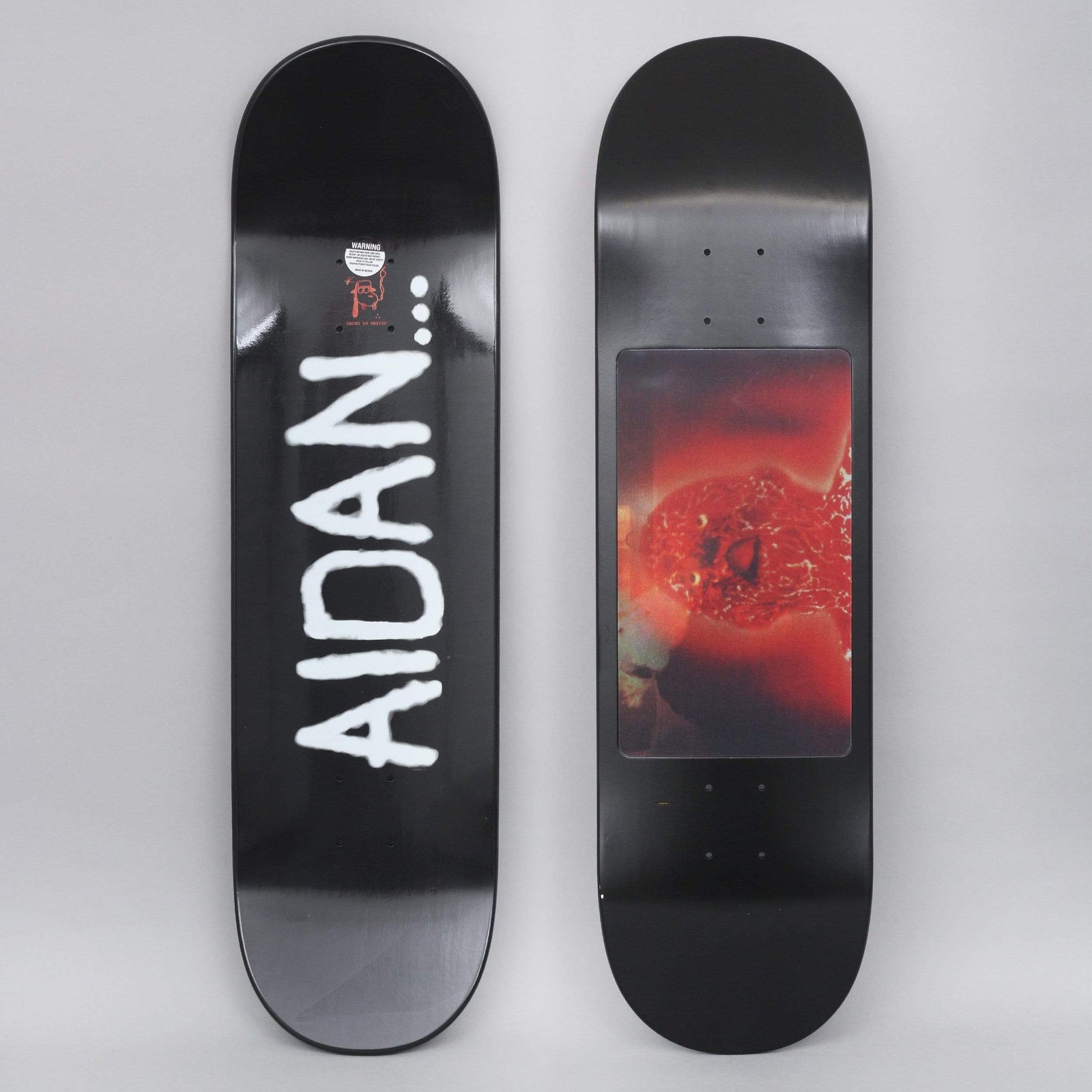 Fucking Awesome Aidan Spray Face Black skateboard deck: Black deck with AIDAN followed by three dots in rough white spray-paint lettering running down the length. The underside shown beside it has a red-tinted photographic panel of a face-like figure.