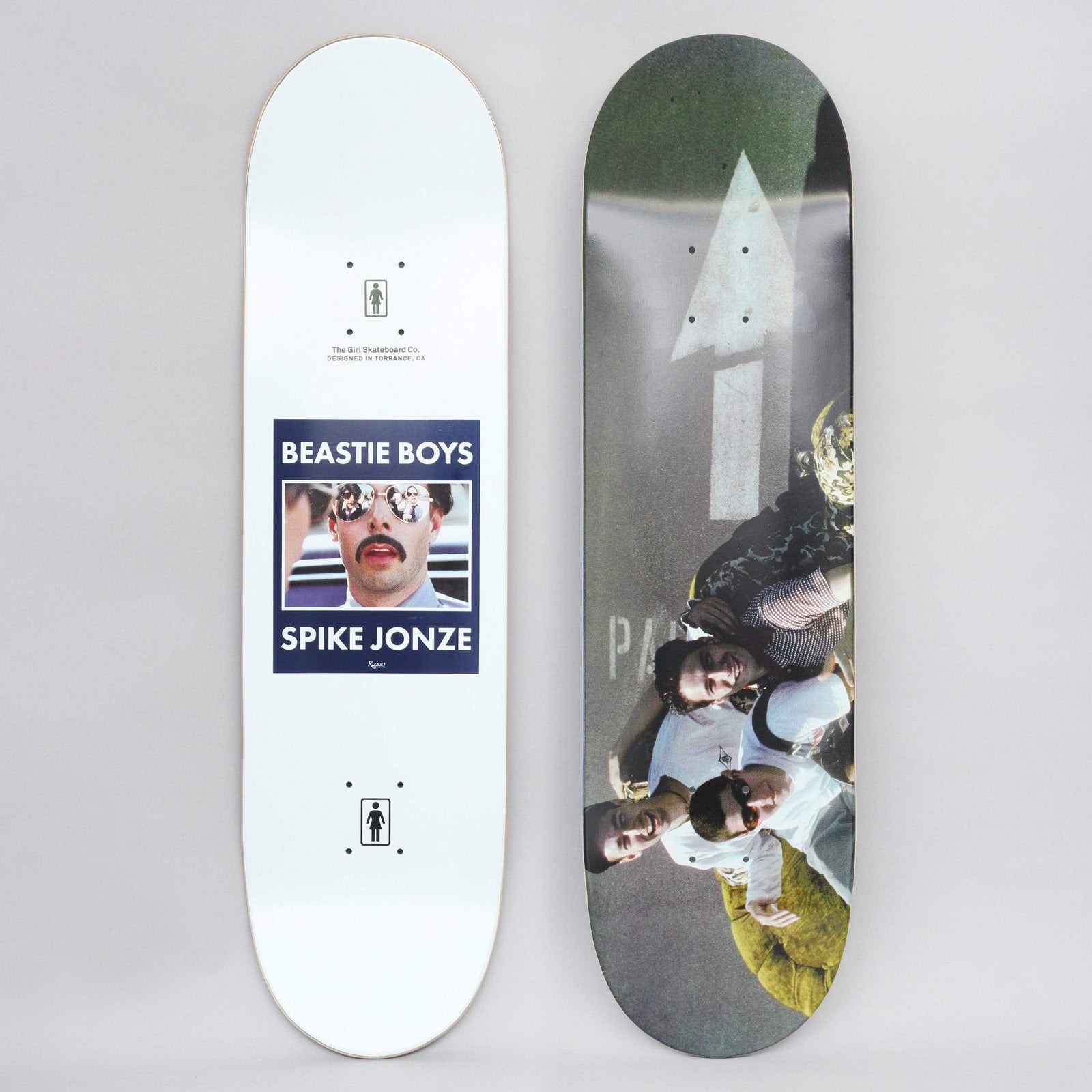 Girl Beastie Boys Spike Jonze #3 skateboard deck: Top graphic shows a colour photo of a group of people in sunglasses lying on tarmac beside a painted white arrow. The other side is white with a framed photo of a moustached man in mirrored sunglasses and a Beastie Boys / Spike Jonze caption.