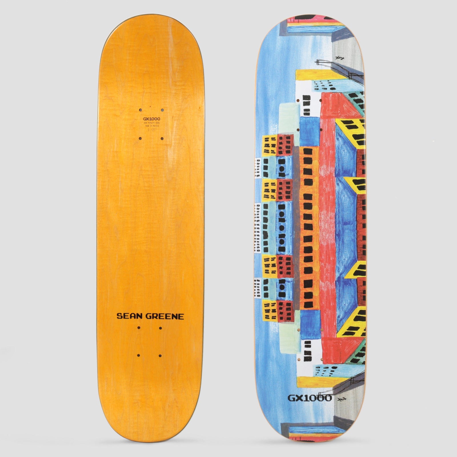 GX1000 Sean Green City skateboard deck: Naive painted cityscape of colourful blocks of flats with black windows and yellow awnings, stacked symmetrically against a blue sky, with the GX1000 logo near the tail.