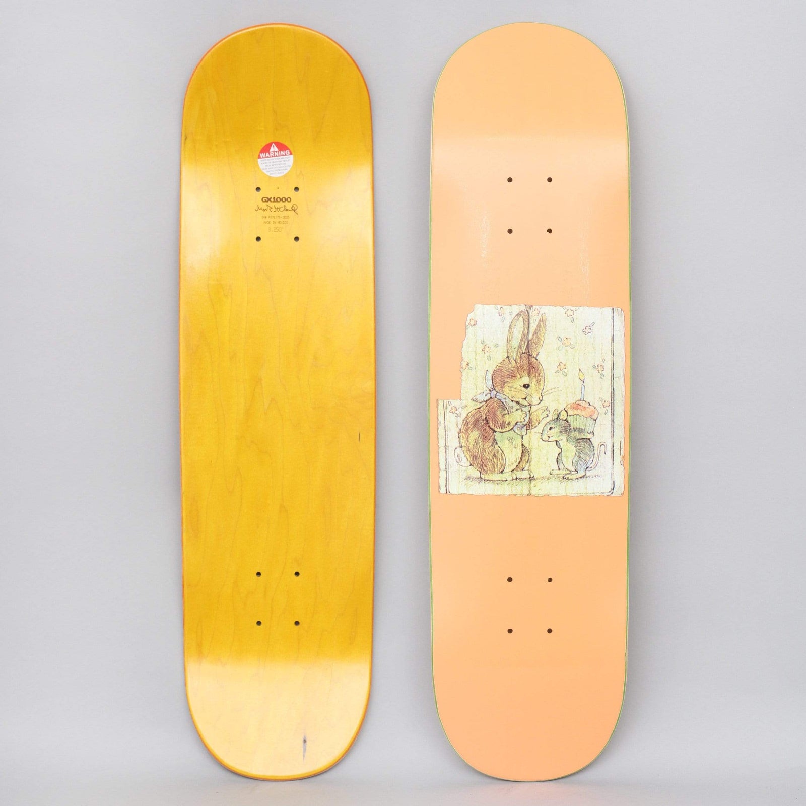 GX1000 Bunny Peach skateboard deck: Peach deck with a small vintage storybook-style illustration of a rabbit and a mouse holding a lit candle on a cupcake, set in a torn-edged panel. A yellow stained underside with GX1000 logo is also shown.