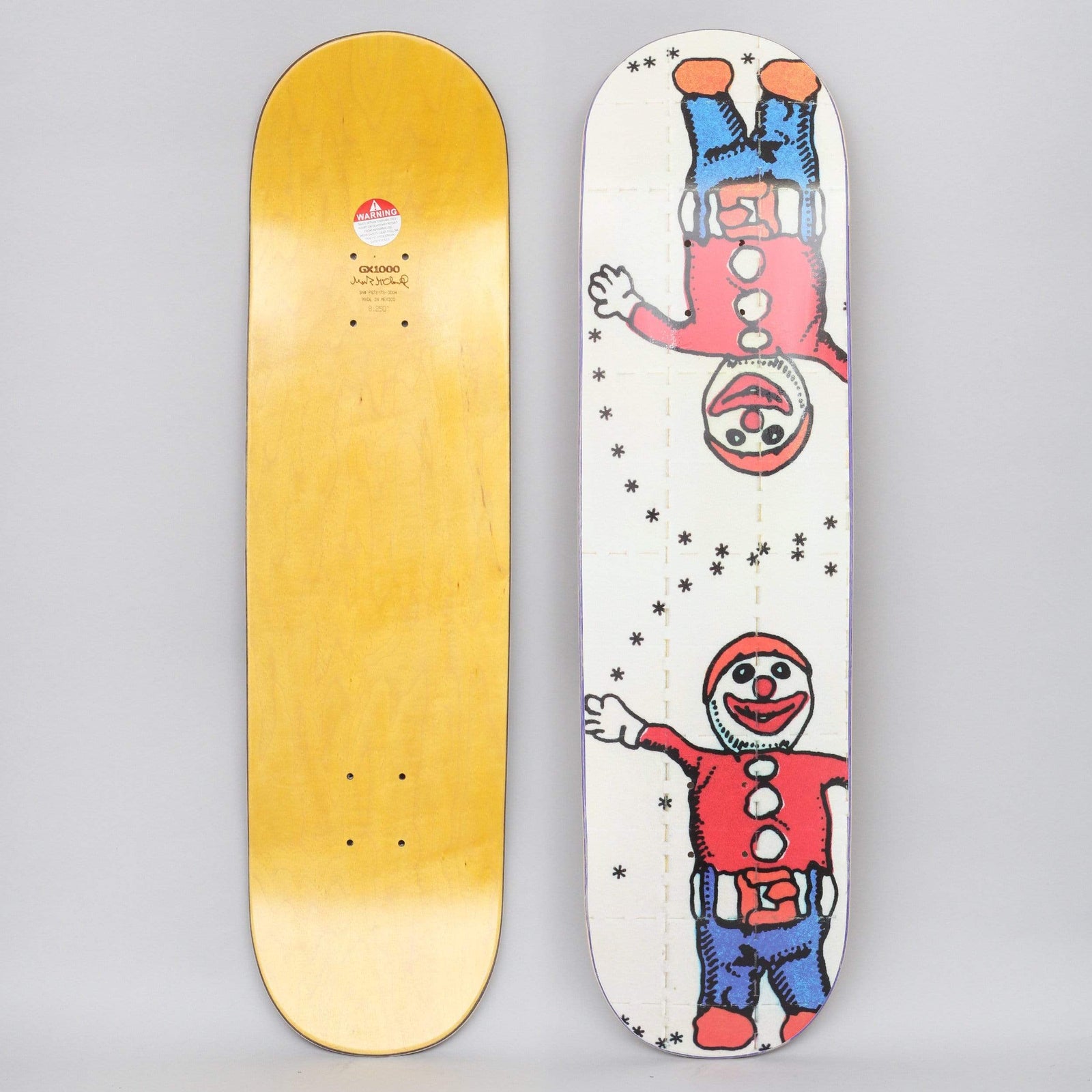 GX1000 Mr Bill skateboard deck: Two cartoon clowns in red tops, blue trousers and red caps, one upright and one upside down, waving, among black asterisk stars on an off-white background. Yellow wood underside shown alongside.