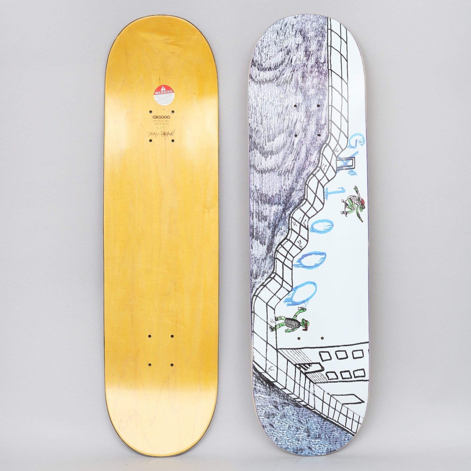 GX1000 Turtle White skateboard deck: Hand-drawn pen illustration of a tiled bowl or wall with a scribbled grey rock face, and two small green turtle skaters riding it. Blue bubble-style 'GX1000' lettering runs down the edge.