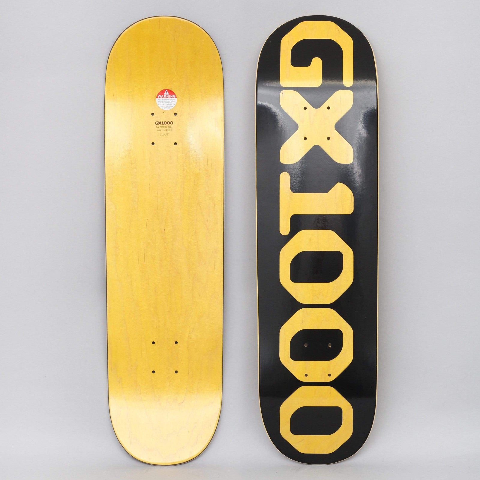 GX1000 OG Logo Yellow skateboard deck: Large yellow stacked block lettering reading GX1000 running down the length of a black deck, the letters reading vertically with the X forming a cross.