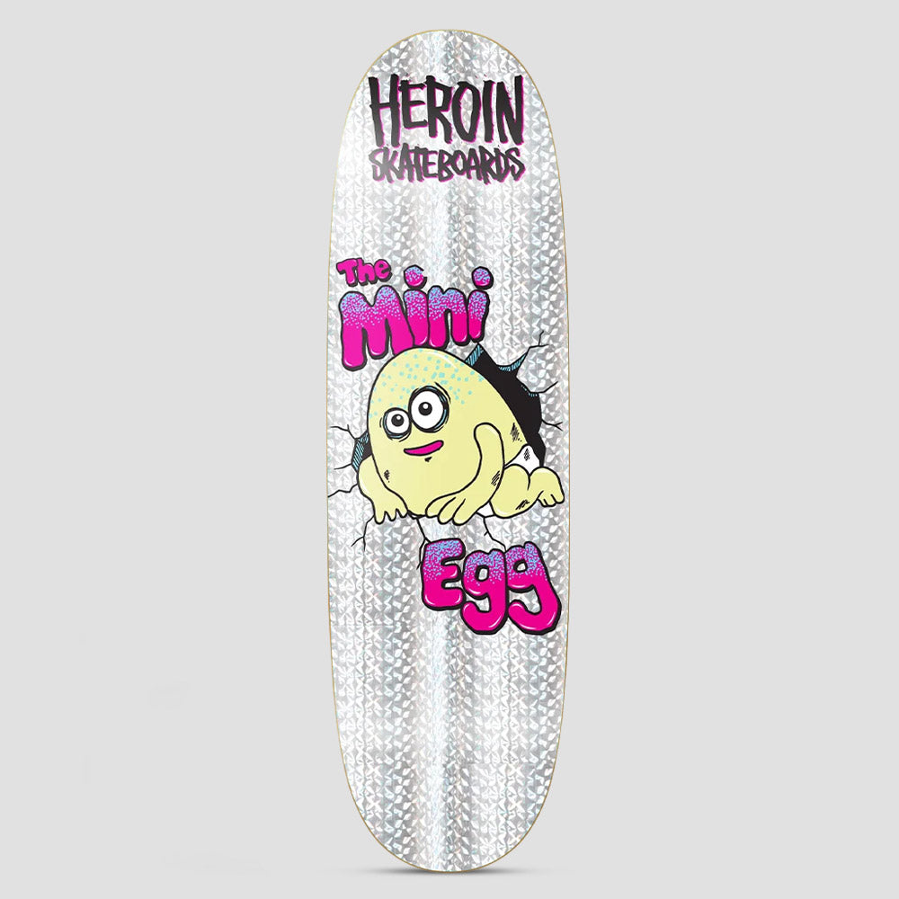 Heroin Mini Egg Holo skateboard deck: Pale yellow cartoon egg creature with wide eyes bursting through a cracked wall, with pink dripping 'The Mini Egg' lettering and Heroin Skateboards logo above, on a silver holographic ground.
