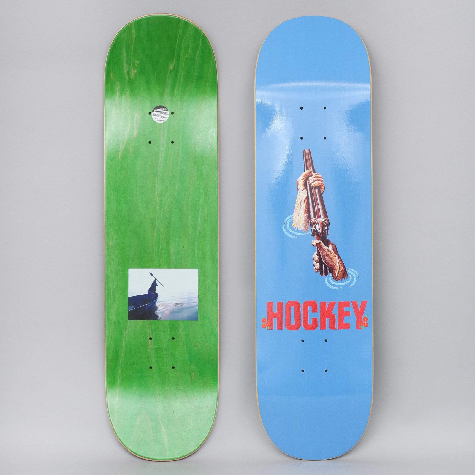 Hockey Andrew Allen Shotgun Blue skateboard deck: Two hands break open a double-barrel shotgun, shown rising out of water with ripples, above red HOCKEY lettering on blue. The underside carries a small photo of a person in a boat.
