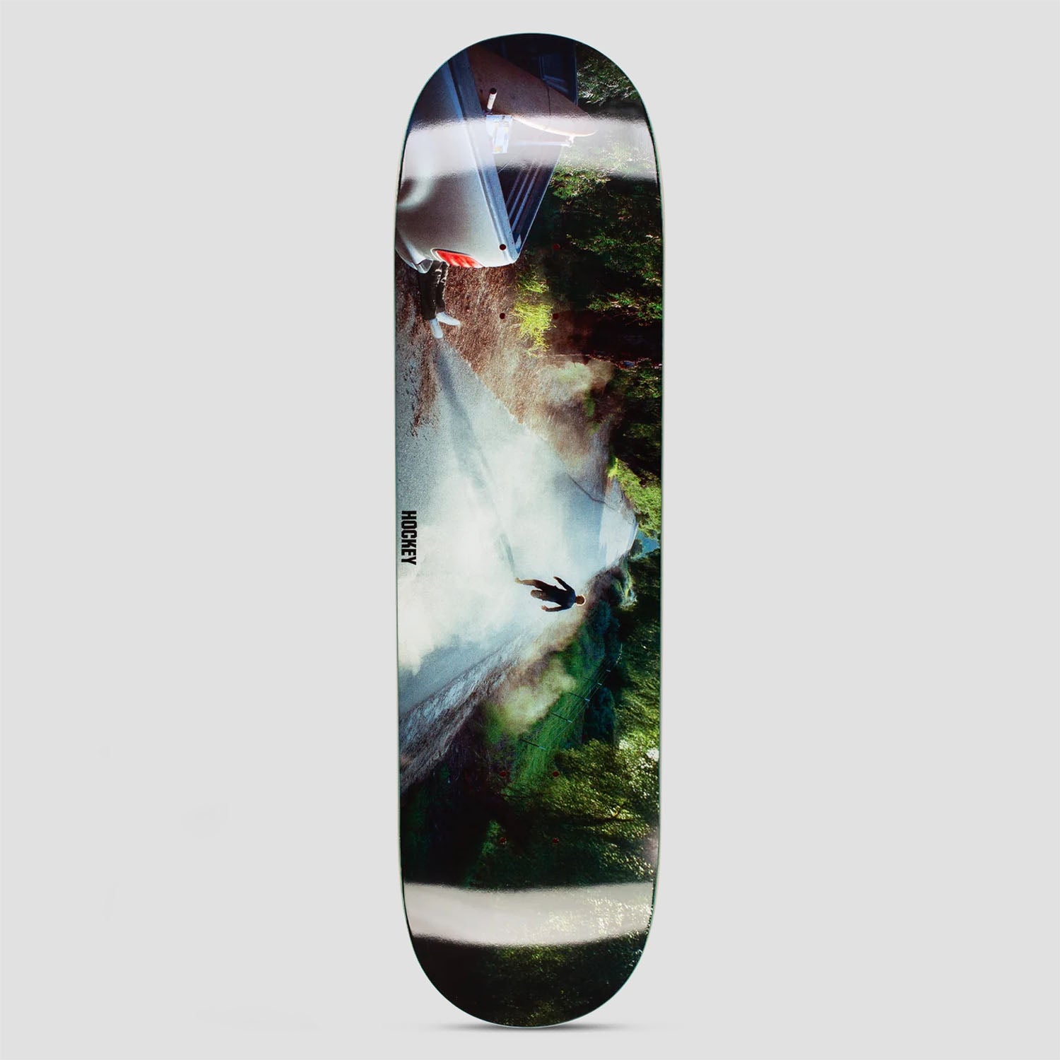 Hockey My Friend The Liar II Diego Todd Shape 2 skateboard deck: Rotated colour photograph of a lone figure standing on a misty road beside a parked vehicle, with trees on one side and light flare streaks across the image. Small Hockey logo at the left edge.