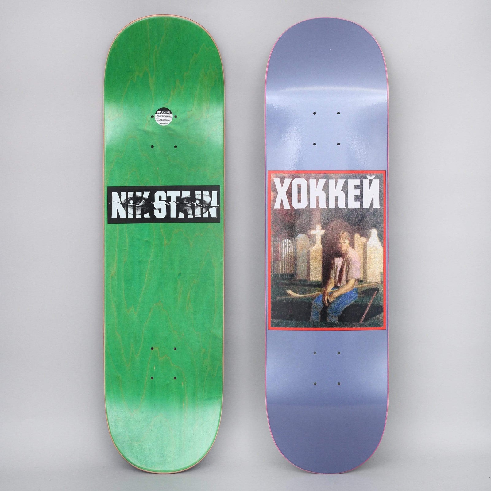 Hockey Nik Stain Metallic Blue skateboard deck: Painted portrait of a long-haired person in a pink shirt holding a hockey stick in a graveyard with crosses and headstones, in a red-bordered box under Cyrillic ХОККЕЙ, on a metallic blue deck.