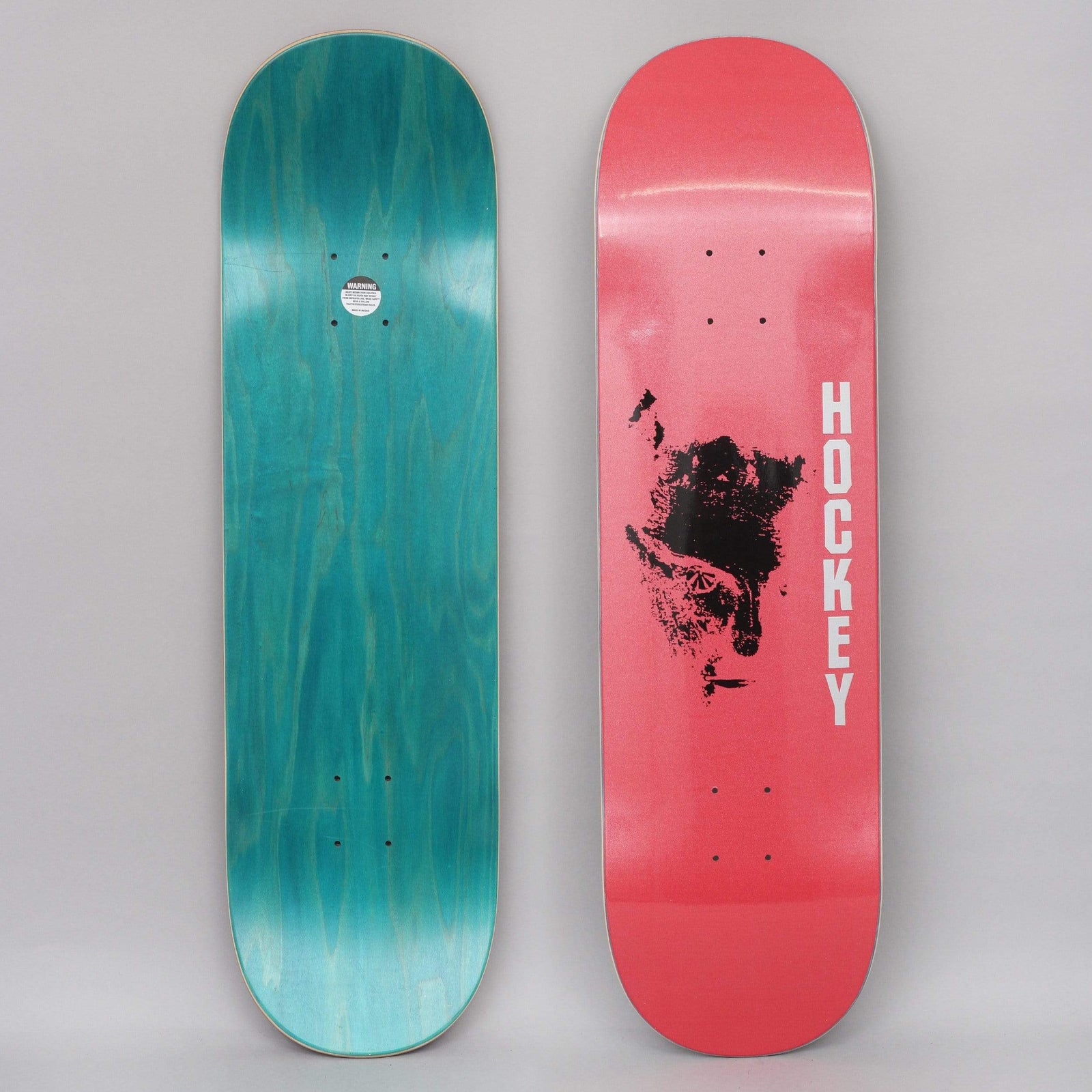 Hockey Chaos Red skateboard deck: Black smudged ink or print blot resembling a face, in the middle of a pink-red deck with vertical white HOCKEY lettering. Underside is teal stain.
