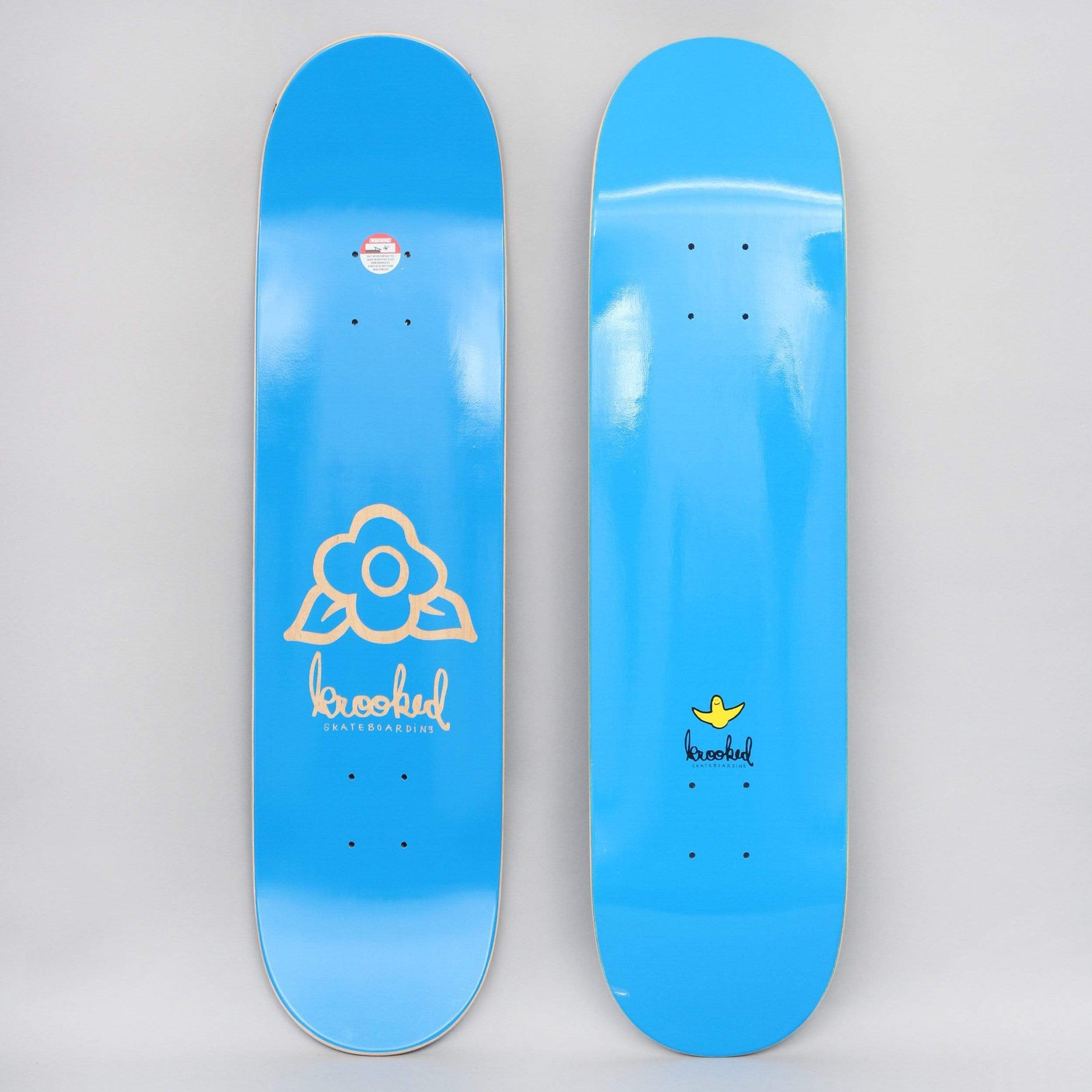 Krooked Ikons 2 PP Blue skateboard deck: Plain bright blue deck shown top and underside. The bottom carries a tan outline flower with leaves above the handwritten krooked skateboarding logo. The top has a small yellow Krooked bird logo and logo.