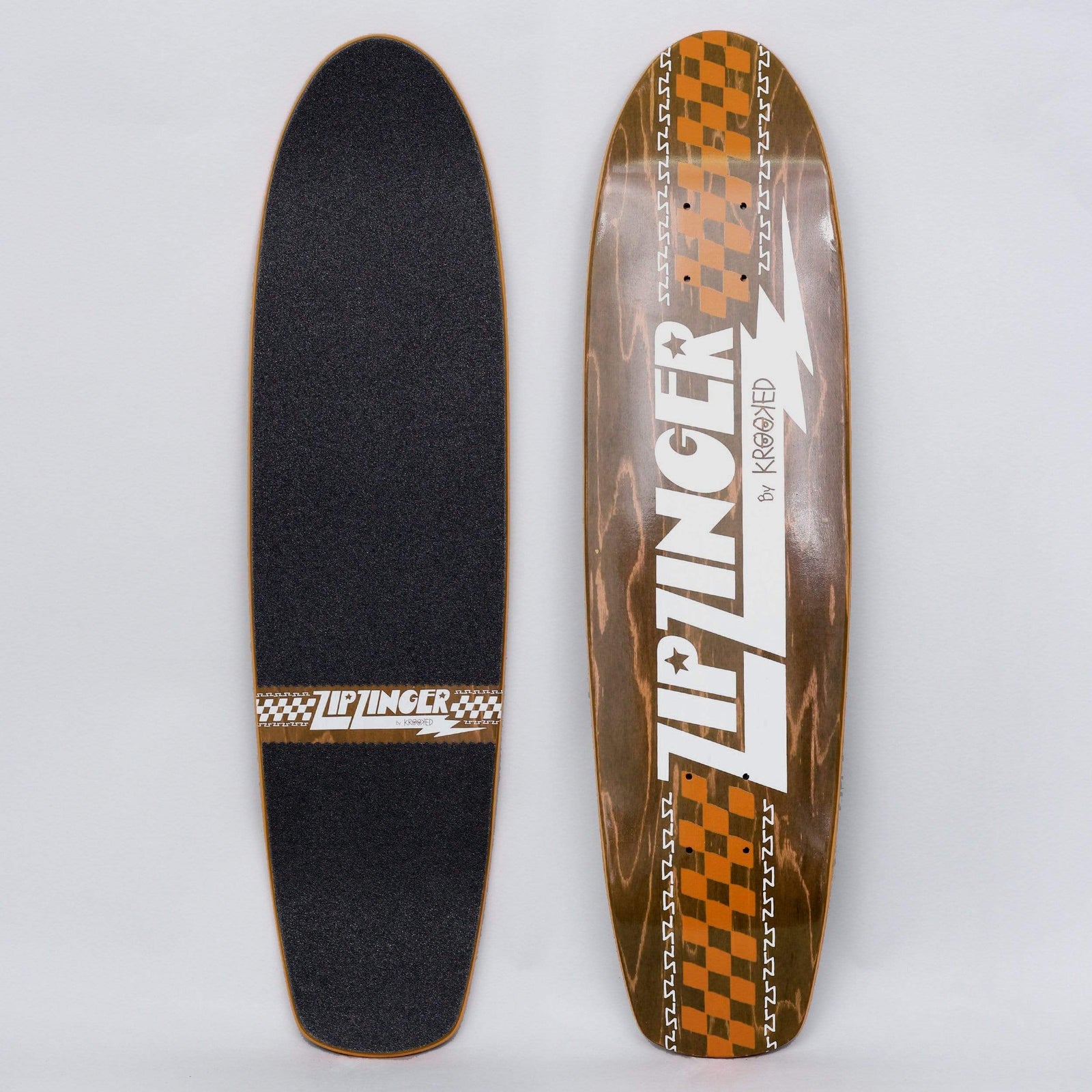 Krooked Zip Zinger Rgb skateboard deck: Small cruiser shape with white Zip Zinger lettering and a lightning bolt, with orange checkerboard bands and zig-zag borders over brown stained wood. Photo also shows the black griptape side.