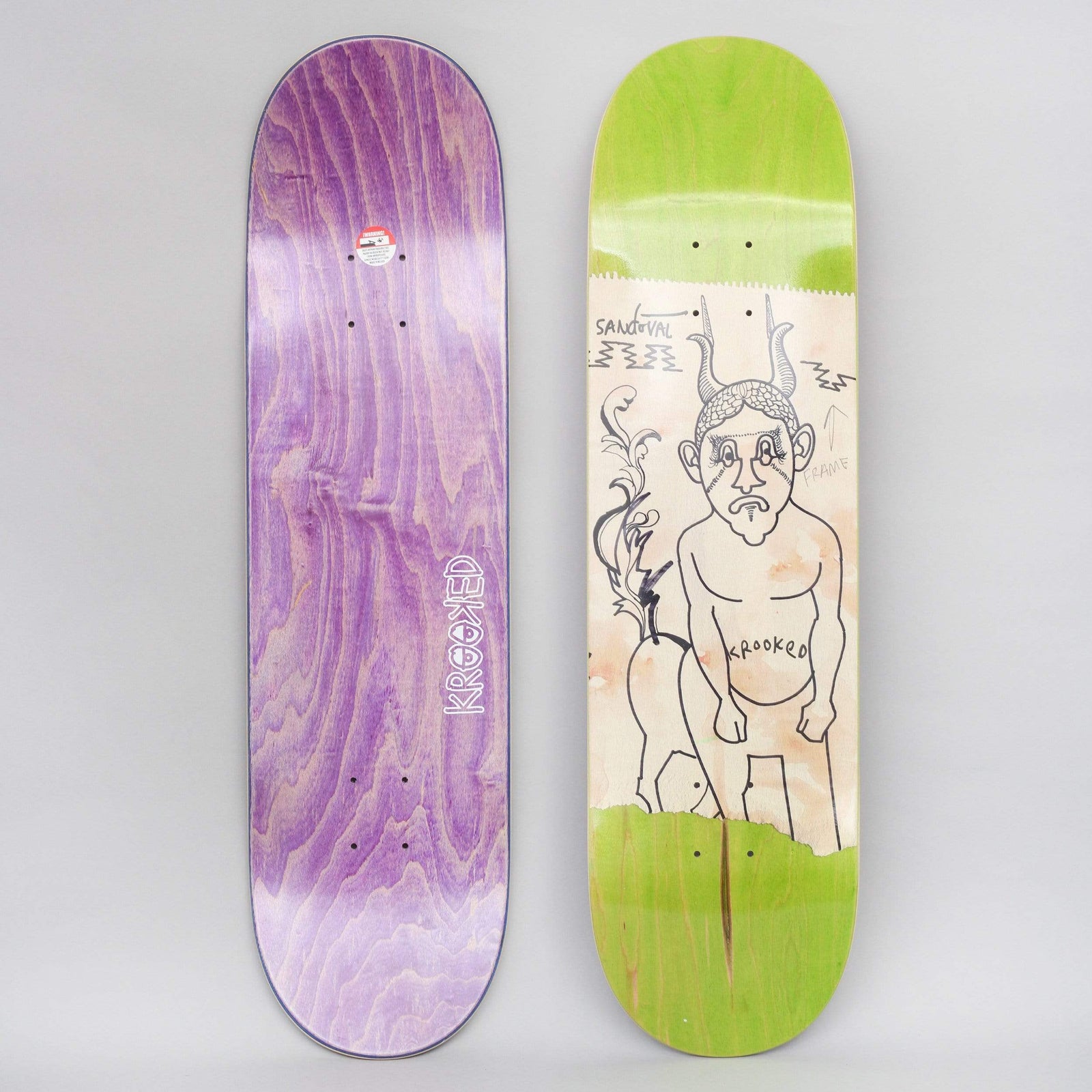 Krooked Sandoval Goat Dude skateboard deck: Loose black line drawing of a sad, horned goat-man with a hairy head standing nude, on a torn cream paper panel over a green stain. The rider's name and 'Fame' with an arrow are scrawled around him. Purple stained bottom shown alongside.