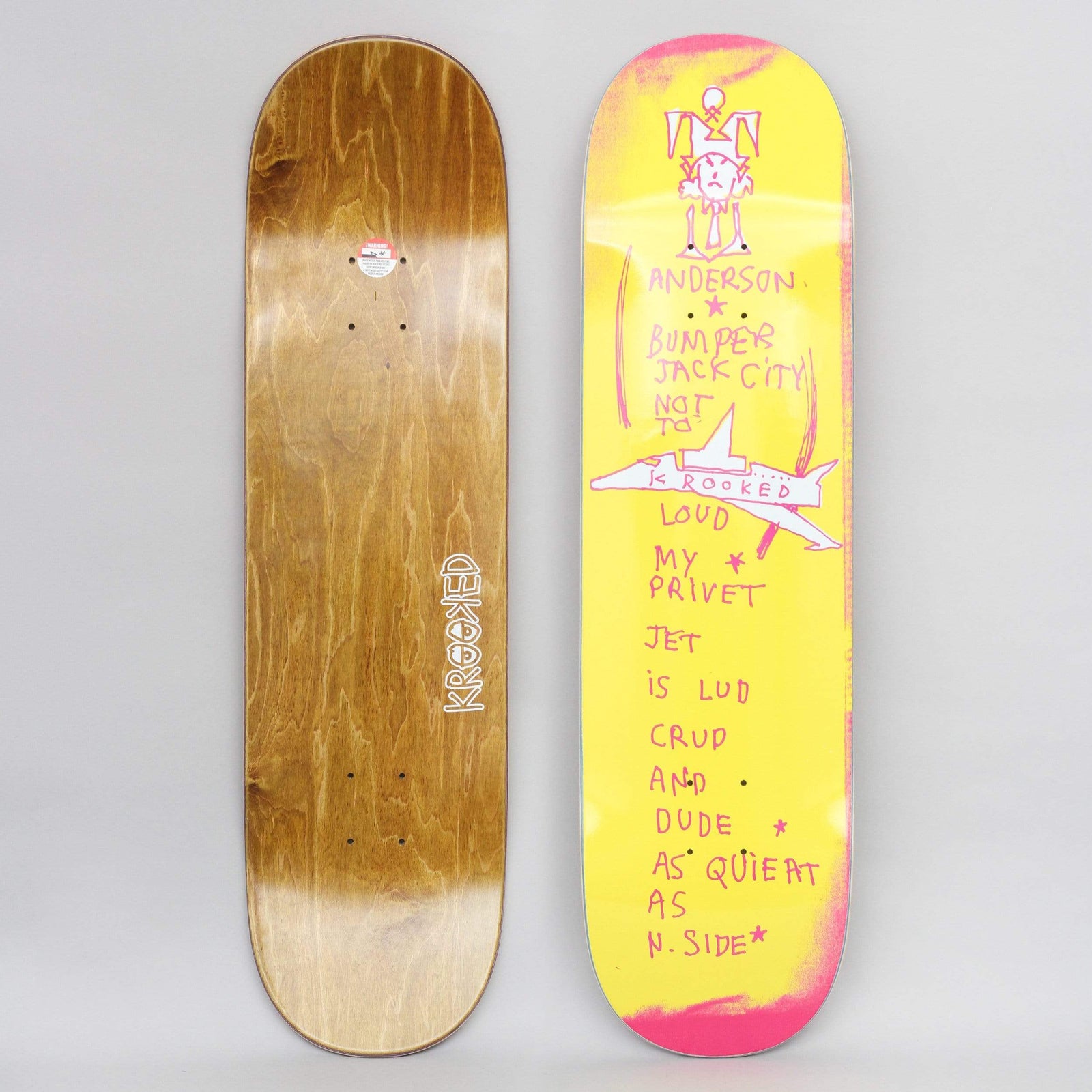 Krooked Anderson Bumper Yellow skateboard deck: Childlike pink scrawl on a yellow deck: a crude figure at the top, handwritten misspelt lines about a loud private jet, and a drawn jet plane across the middle. Brown wood bottom shown alongside.