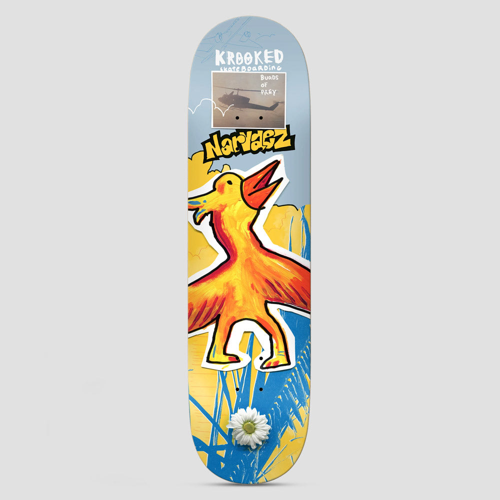 Krooked Narvaez Burds Multi skateboard deck: A childlike painted orange and yellow bird with an open beak stands against a pale blue and yellow collage with blue grass. A small photo of a helicopter captioned Burds of Prey sits near the top, and a white daisy is at the tail.