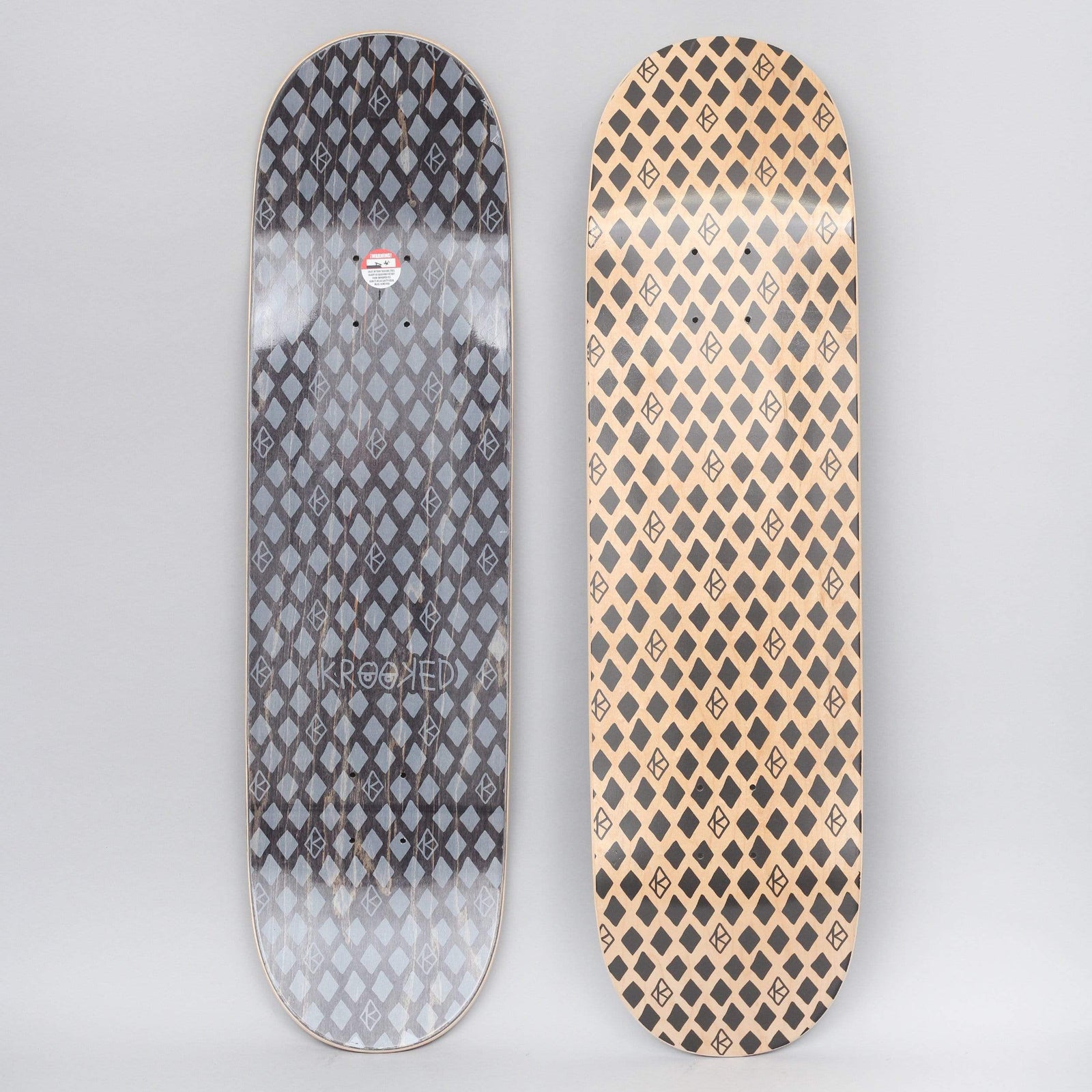 Krooked Dymonds Black skateboard deck: Repeating all-over pattern of black diamond shapes interspersed with small outlined Krooked eye logos on bare natural wood. The underside shows the same pattern in grey on black with a Krooked wordmark.
