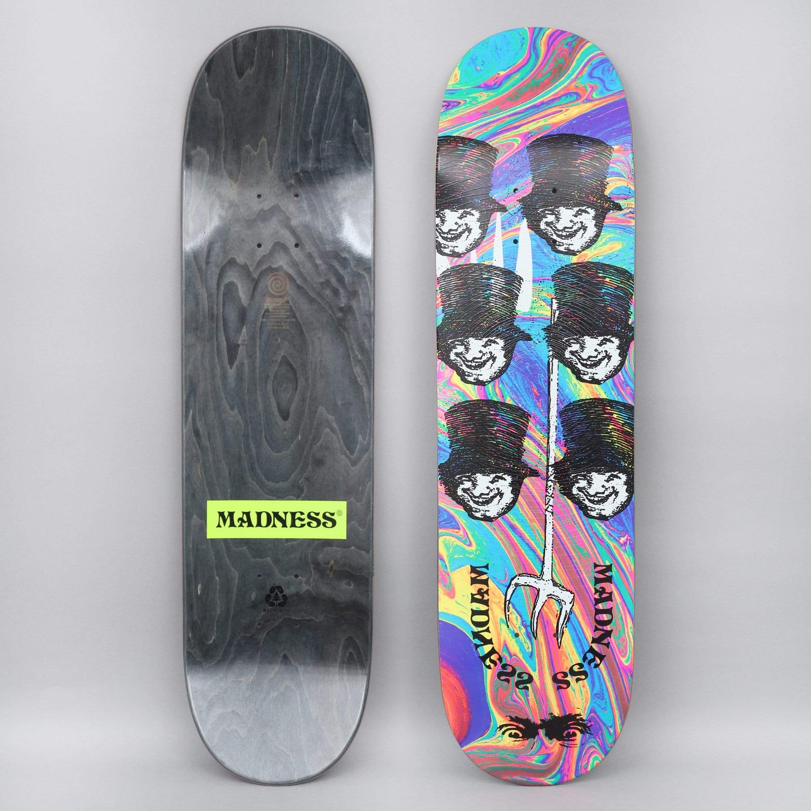 Madness Mayhem Popsicle skateboard deck: Six black top-hatted grinning faces in two columns, with a white trident through the middle, on a swirling rainbow oil-slick background. Madness lettering curved at the foot. Wood underside shown with a green logo.