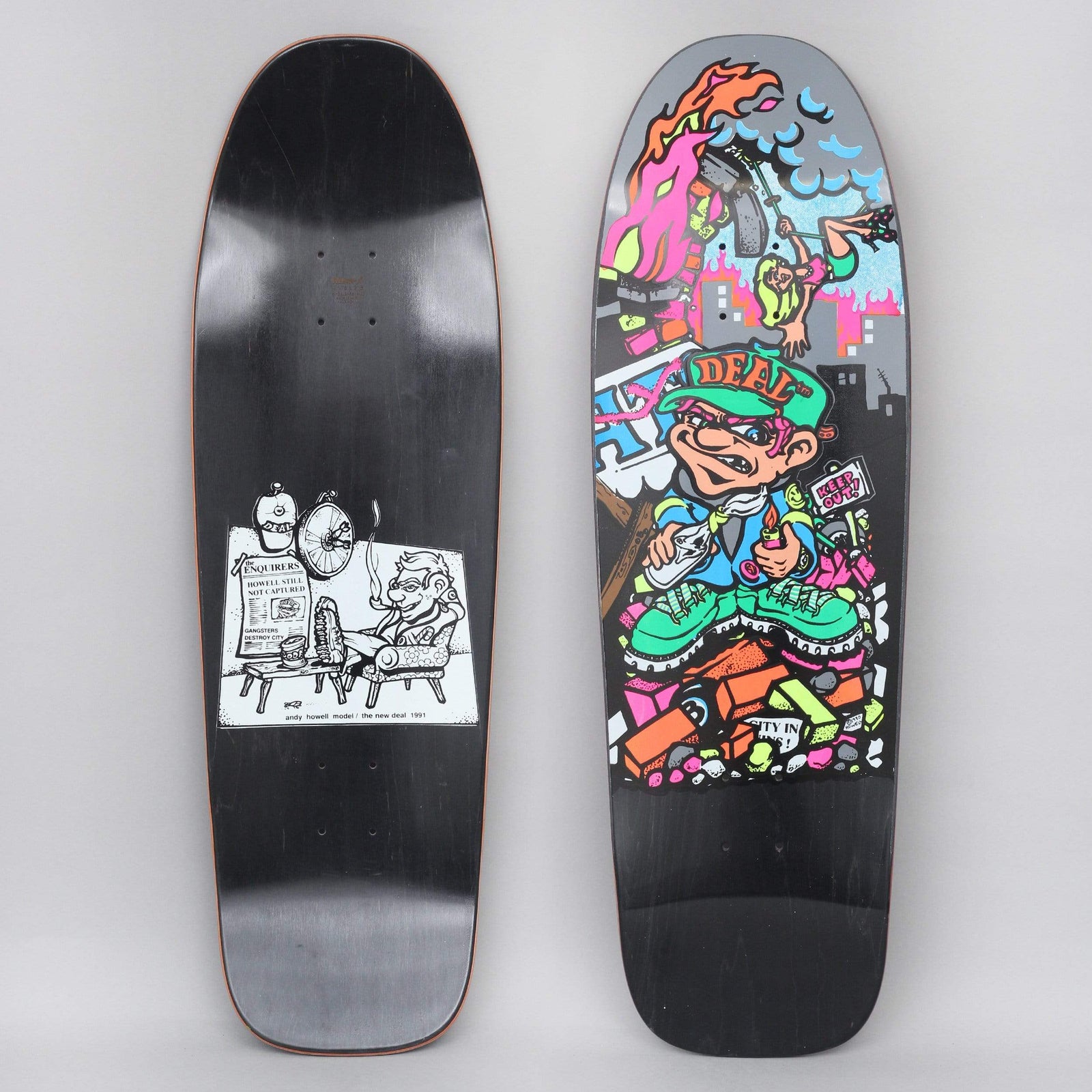 New Deal Howell Molotov Kid SP Black skateboard deck: A cartoon kid in a Deal cap and green boots lighting a petrol bomb on a pile of bricks, with a burning city and a falling skater behind. The underside shows a black and white cartoon of a man in an armchair.