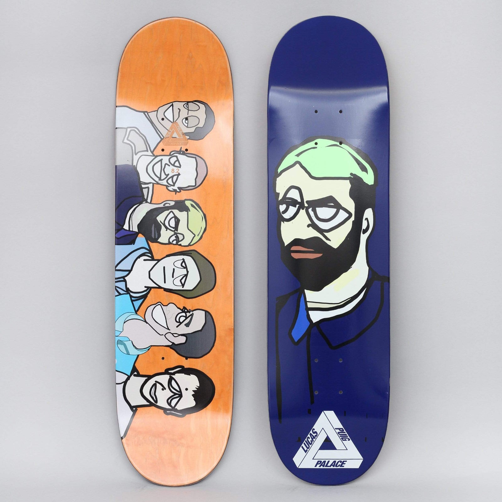 Palace Lucas Pro S20 Navy skateboard deck: Navy deck with a cartoon portrait of a bearded man with glasses and pale green hair, wearing a dark collared shirt, above the Palace triangle logo. The other deck shows a row of six stylised faces on orange.