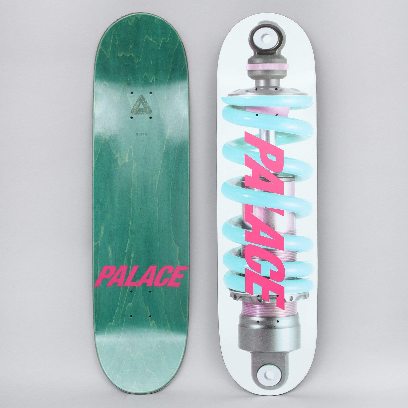 Palace Shock White / Pink skateboard deck: White deck showing a photographic shock absorber with a pale blue coil spring, with the Palace name in slanted pink capitals across it. The underside, green with pink Palace text, is shown alongside.