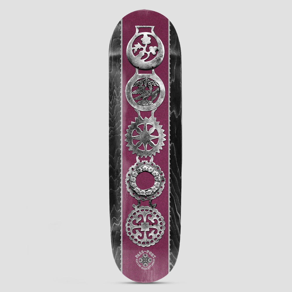 Passport Brasses Pro Series Matlok skateboard deck: A vertical column of five ornate silver horse brasses on a burgundy stripe, between black stained wood-grain edges. The Pass~Port logo and rider name sit at the tail.