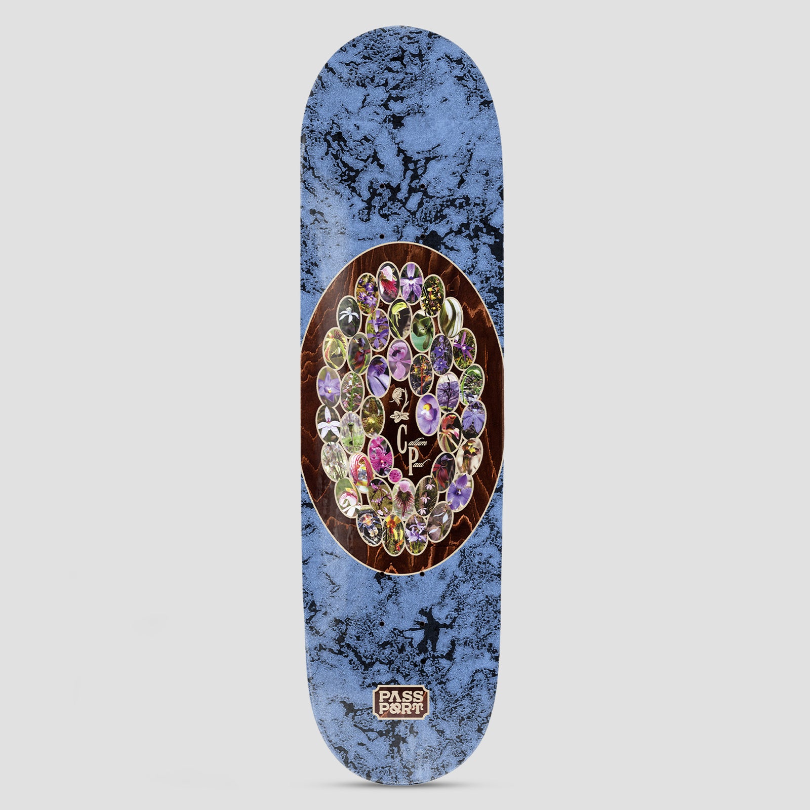 Passport Callum Yearbook Series skateboard deck: A brown wood-grain oval contains a ring of small oval photographs of purple, yellow and green orchids around initials. The surround is marbled blue, and a small Passport logo sits near the tail.