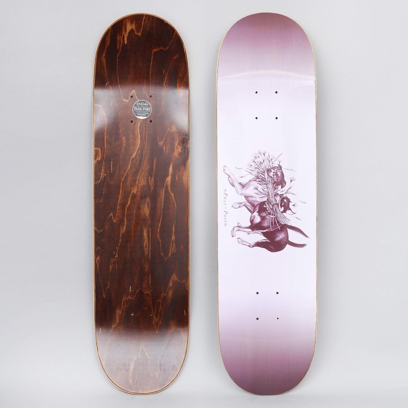 Passport Doggo Lavender skateboard deck: A lavender deck with a dark plum engraving-style drawing of two dogs wrestling, with a bunch of flowers among them. The Pass-Port name is written beside it. Top and underside are shown.