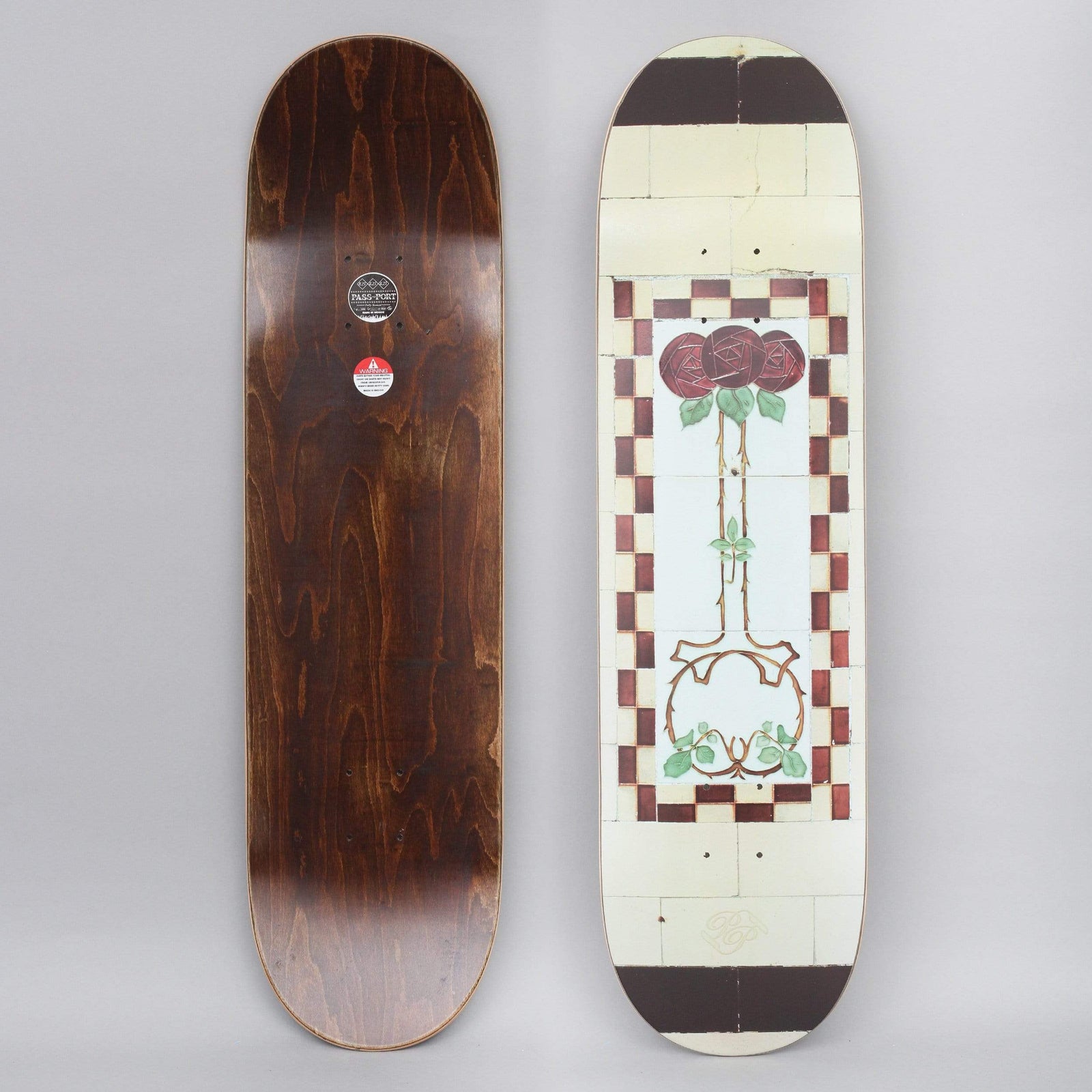 Passport Tile Life Cream skateboard deck: Photographic print of an old cream tile panel with a central art nouveau red rose on a thorny stem inside a checkered maroon and white border. Dark brown bands cap each end.