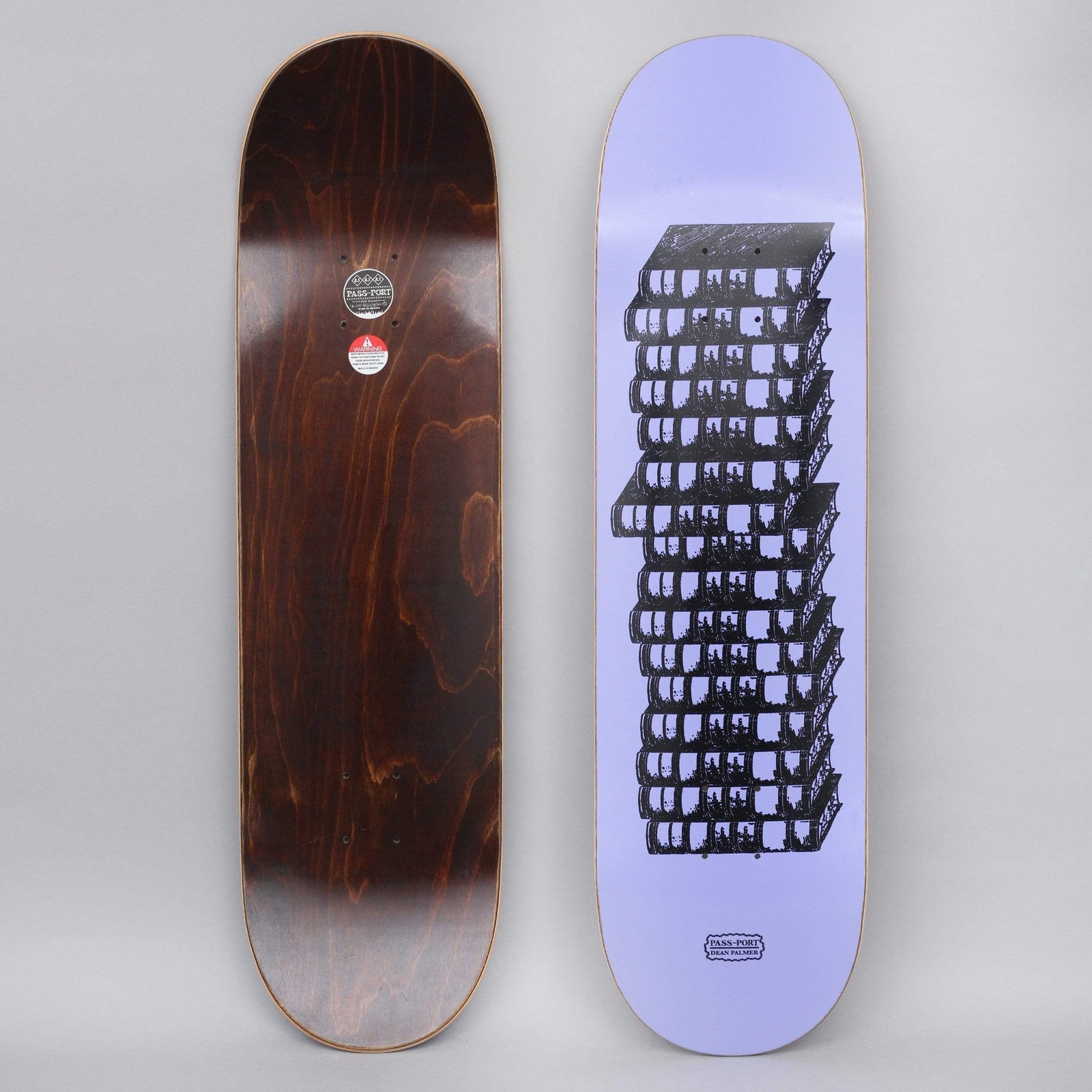 Passport Dean Palmer Pro Series Purple skateboard deck: Lilac deck with a black linework illustration of a tall stack of books or blocks, drawn with dense windows or shelves and slightly offset, with a small Passport name plate near the tail.