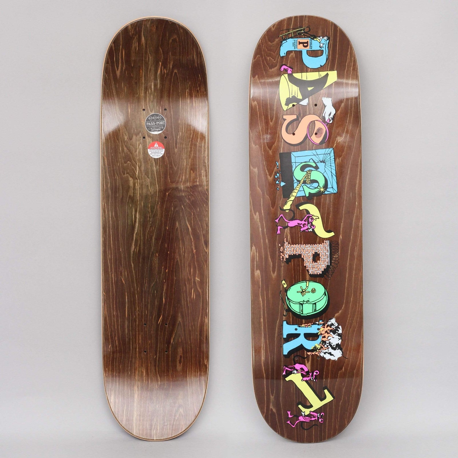 Passport Loot Solid Brown skateboard deck: PASS-PORT spelled vertically in mismatched letter blocks in pastel colours, each decorated with small cartoon figures, tools and objects, over a brown wood-stain deck.
