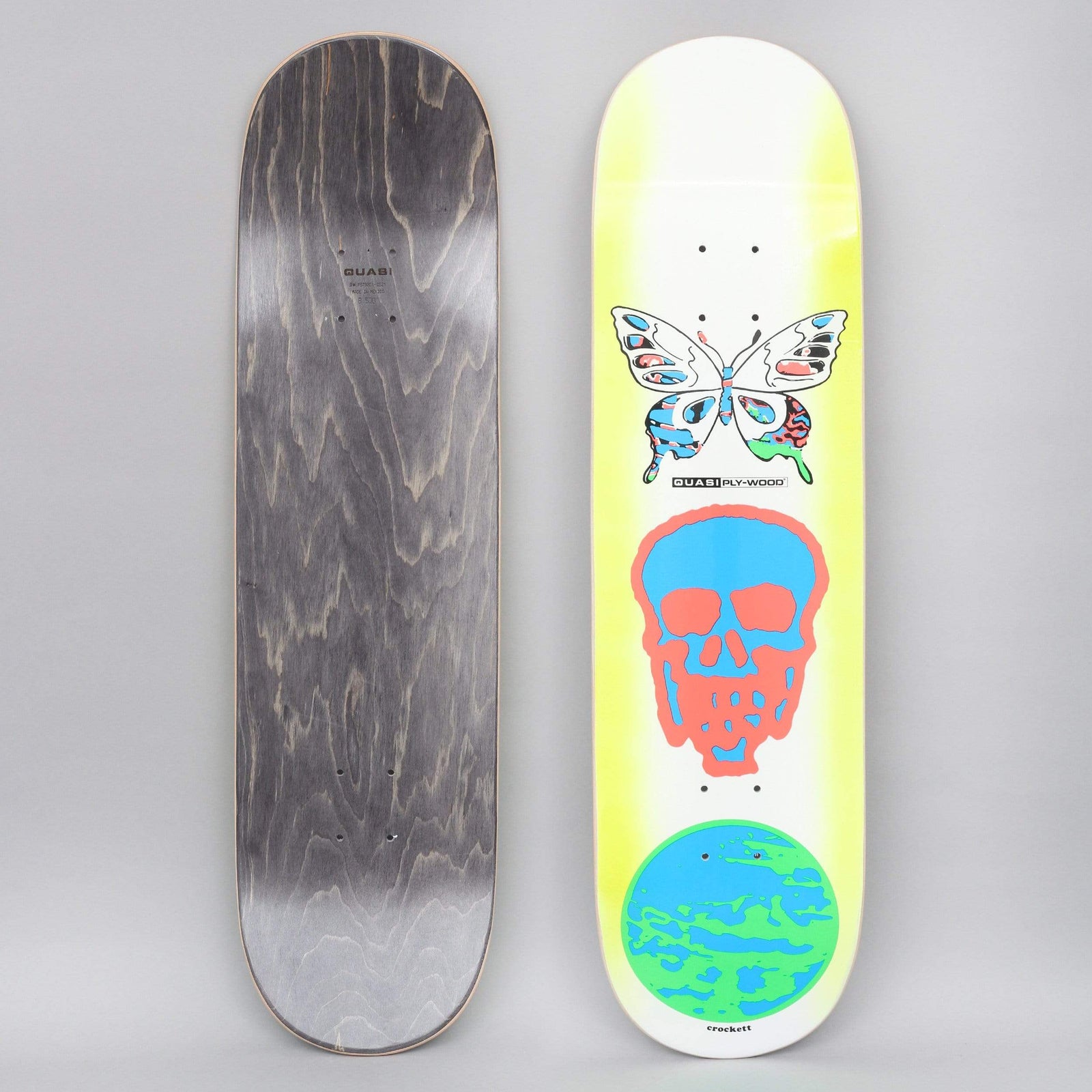 Quasi Quasi 8.5 Crockett Mode skateboard deck: Three stacked symbols on a white deck fading to yellow-green at the edges: a pastel butterfly with abstract wings, a blue skull outlined in coral, and a blue and green globe. The Quasi Ply-Wood logo and rider name are small.