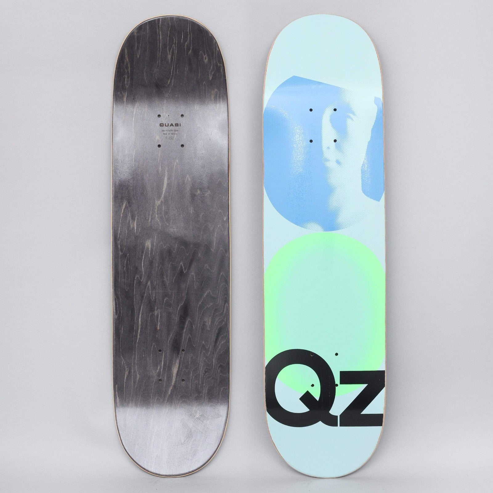 Quasi Quasi 8.25 QZ 101 Blue skateboard deck: A pale blue deck with a blue halftone profile of a face in a circle above a green glowing circle, with a large black QZ lettering at the bottom. The underside is black-stained with small Quasi text.