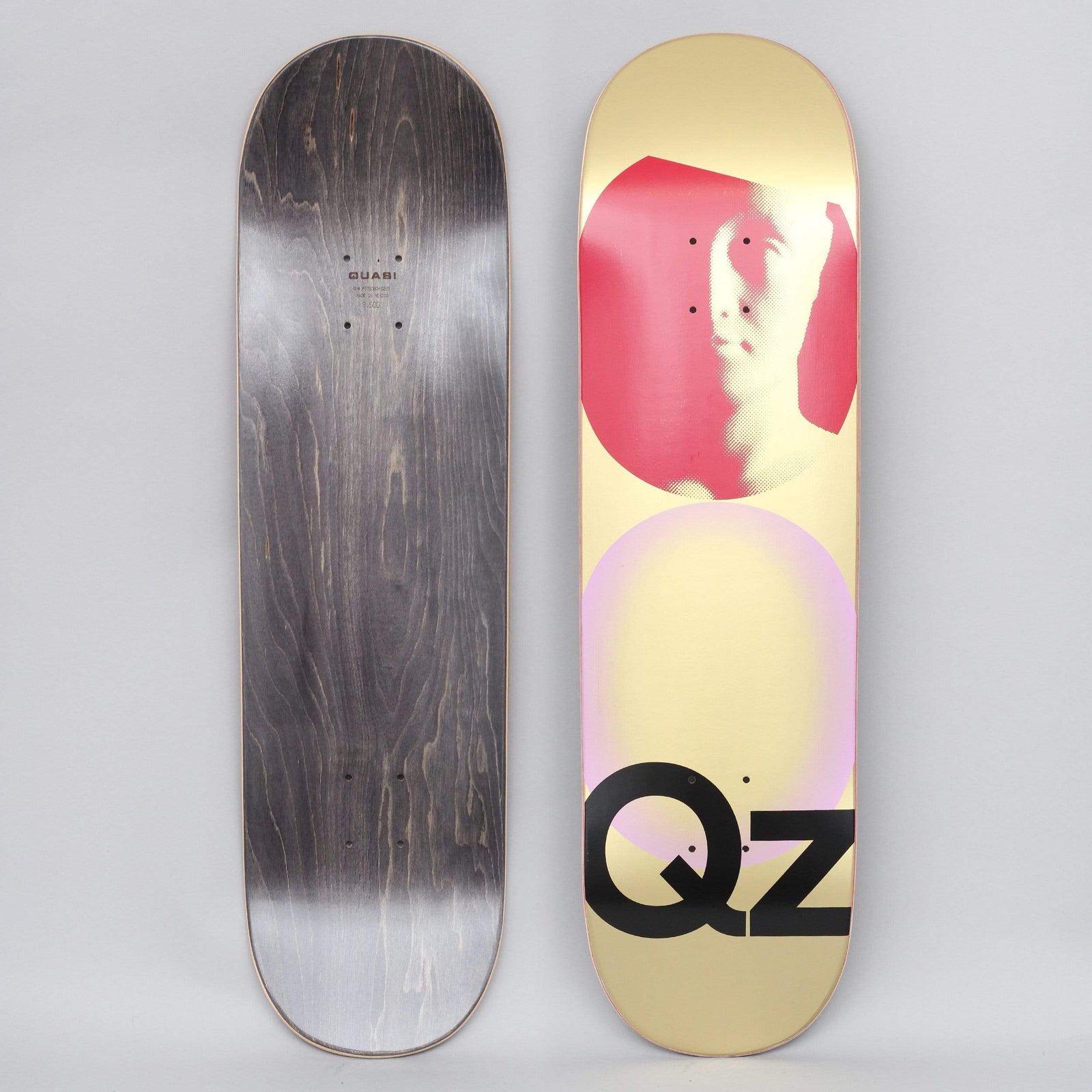 Quasi Quasi 8.5 QZ 101 Gold skateboard deck: A halftone photo of a face inside a red circle above a pale pink circle, with large black QZ letters, on a metallic gold deck. The black-stained underside is shown alongside.