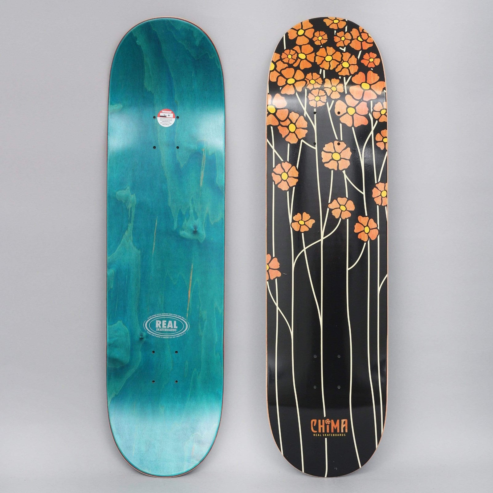 Real Chima Poppy Fields Redux skateboard deck: Tall thin cream stems topped with orange poppies rise across a black deck, the flowers clustering at the nose. The Chima name and Real logo sit at the tail; the teal-stained underside is shown beside it.