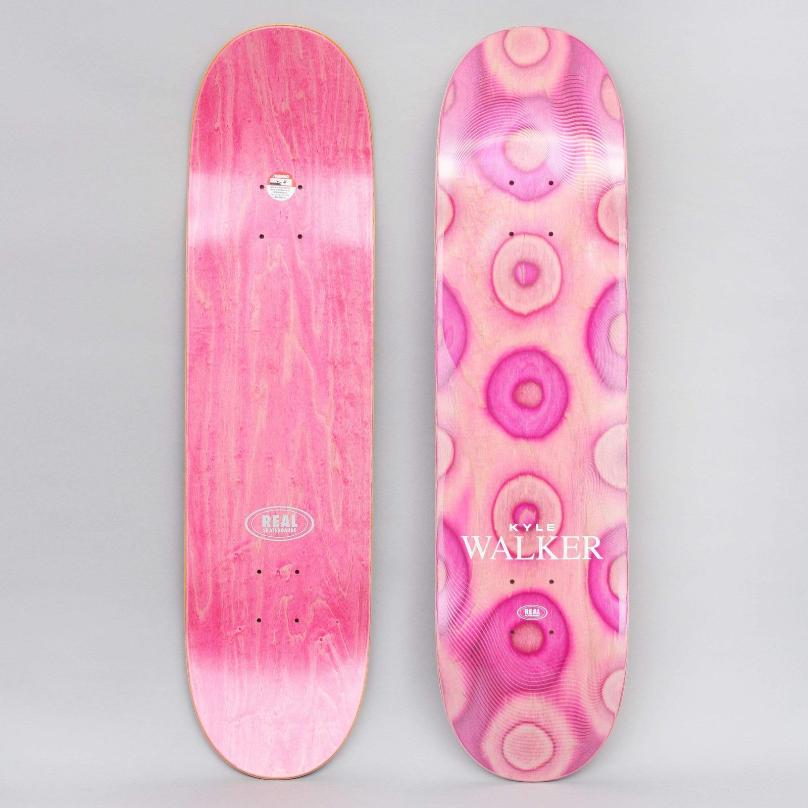 Real Kyle Eclipse Ltd II skateboard deck: Concentric ring pattern in pink and pale pink repeated down the deck like warped circles, with the rider name Kyle Walker in white serif lettering and a small Real logo. Underside is pink stain with a Real oval.