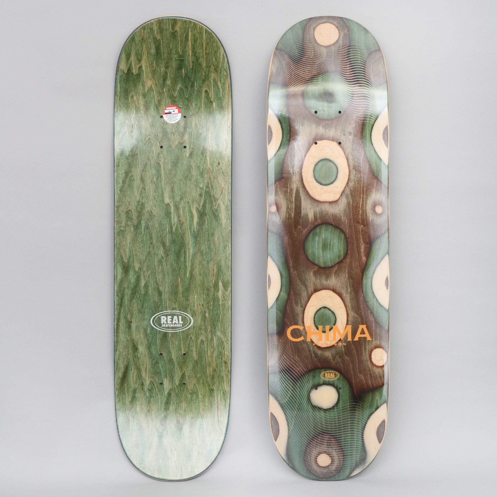 Real Chima Eclipse Ltd II Full skateboard deck: Deck made of engraved layered veneers showing concentric rings and oval shapes in green, brown and natural wood, with orange CHIMA lettering. The underside is green-stained with a Real oval logo.
